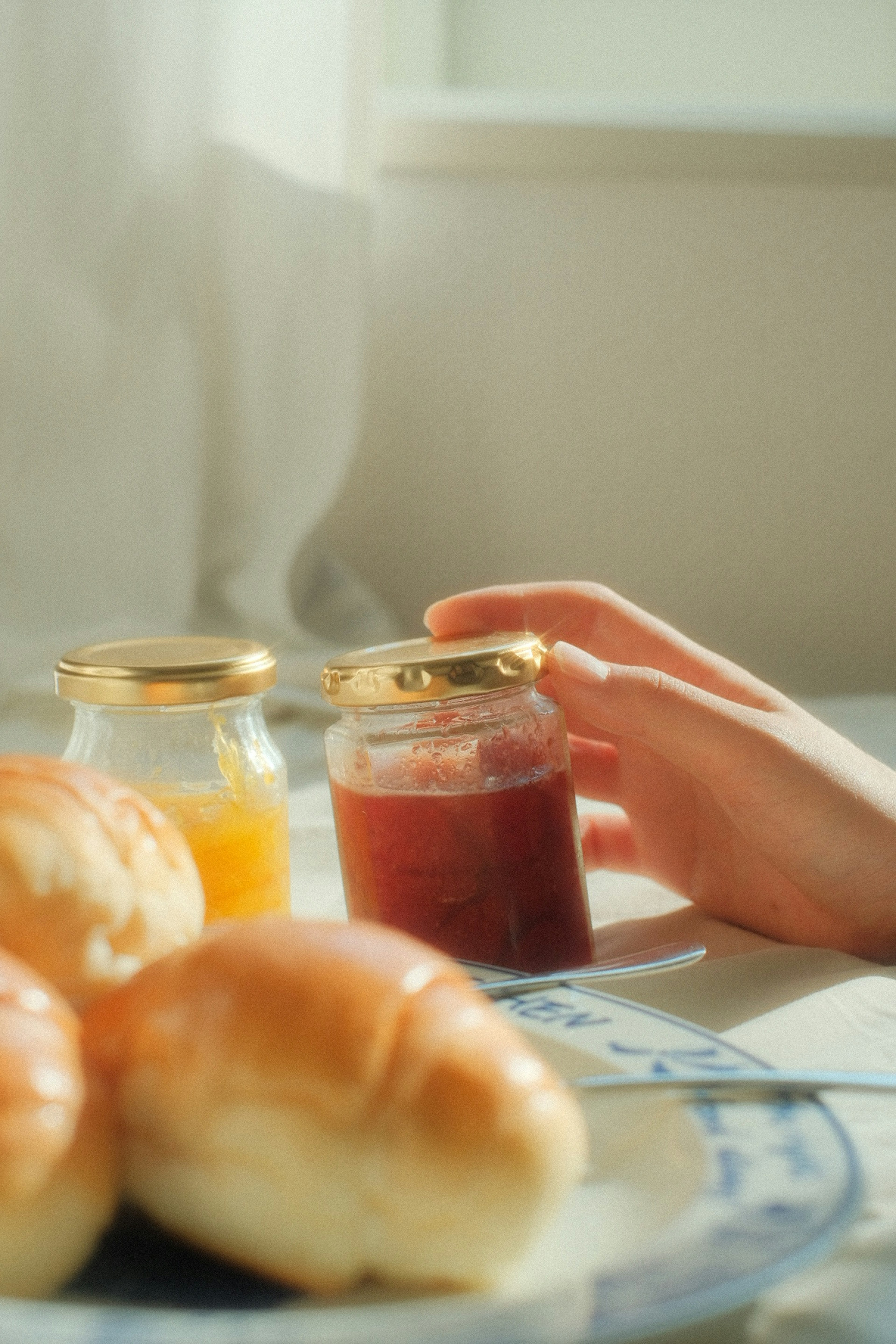 Close-up of a hand reaching for jars of jam next to fresh bread rolls