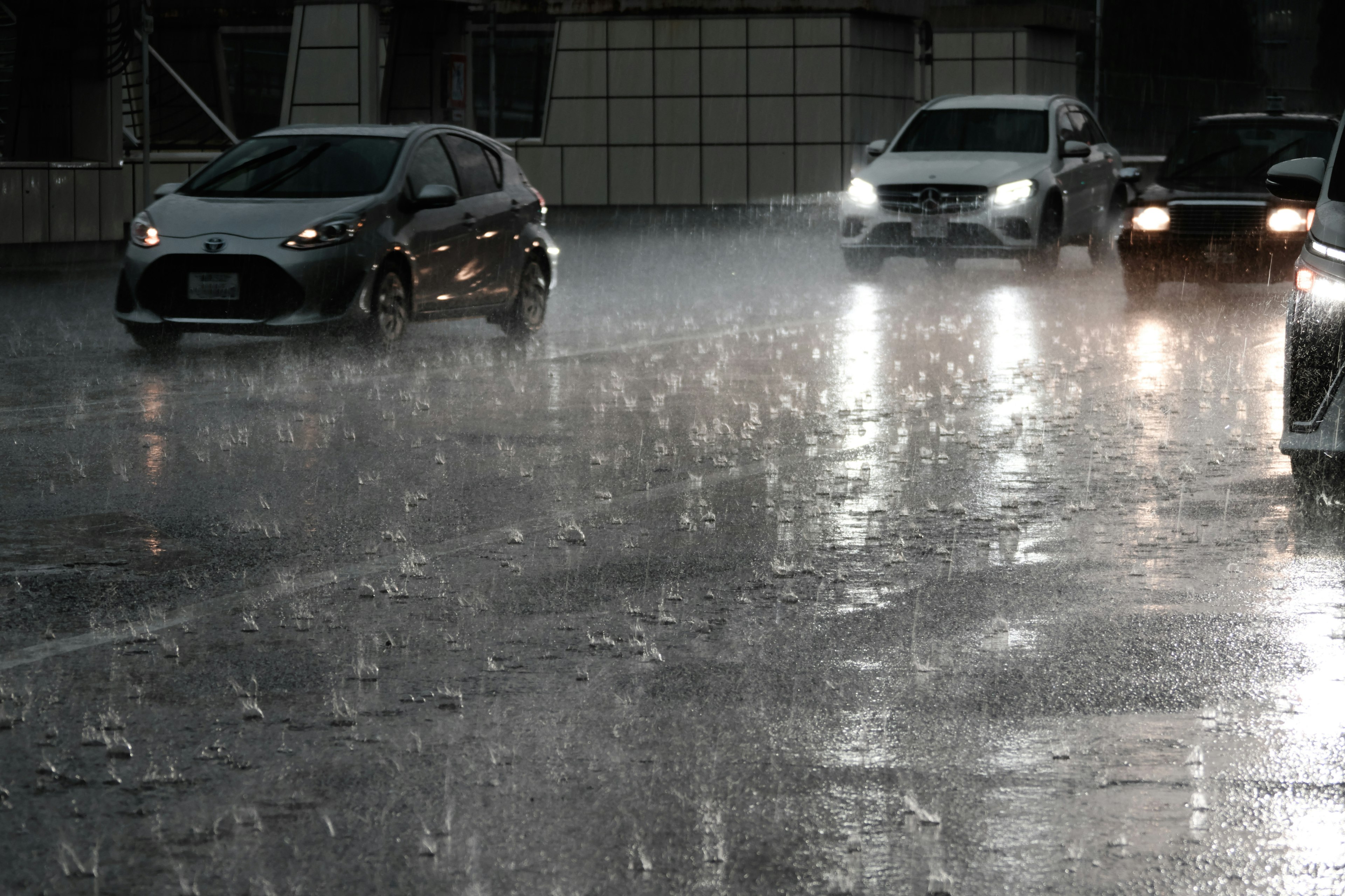 Coches conduciendo bajo una fuerte lluvia con charcos en la calle