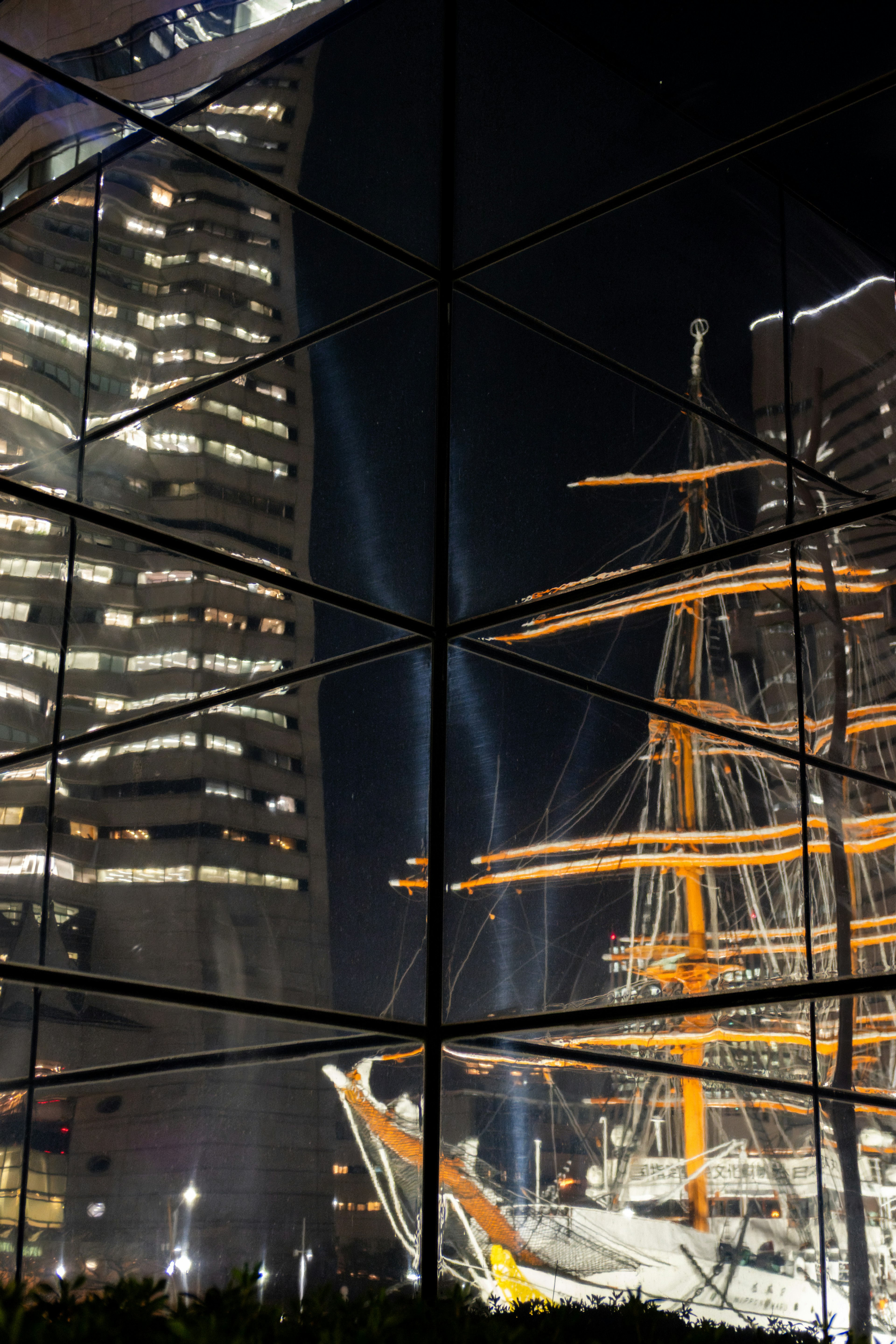 Reflection of a historic sailing ship against modern city skyscrapers at night