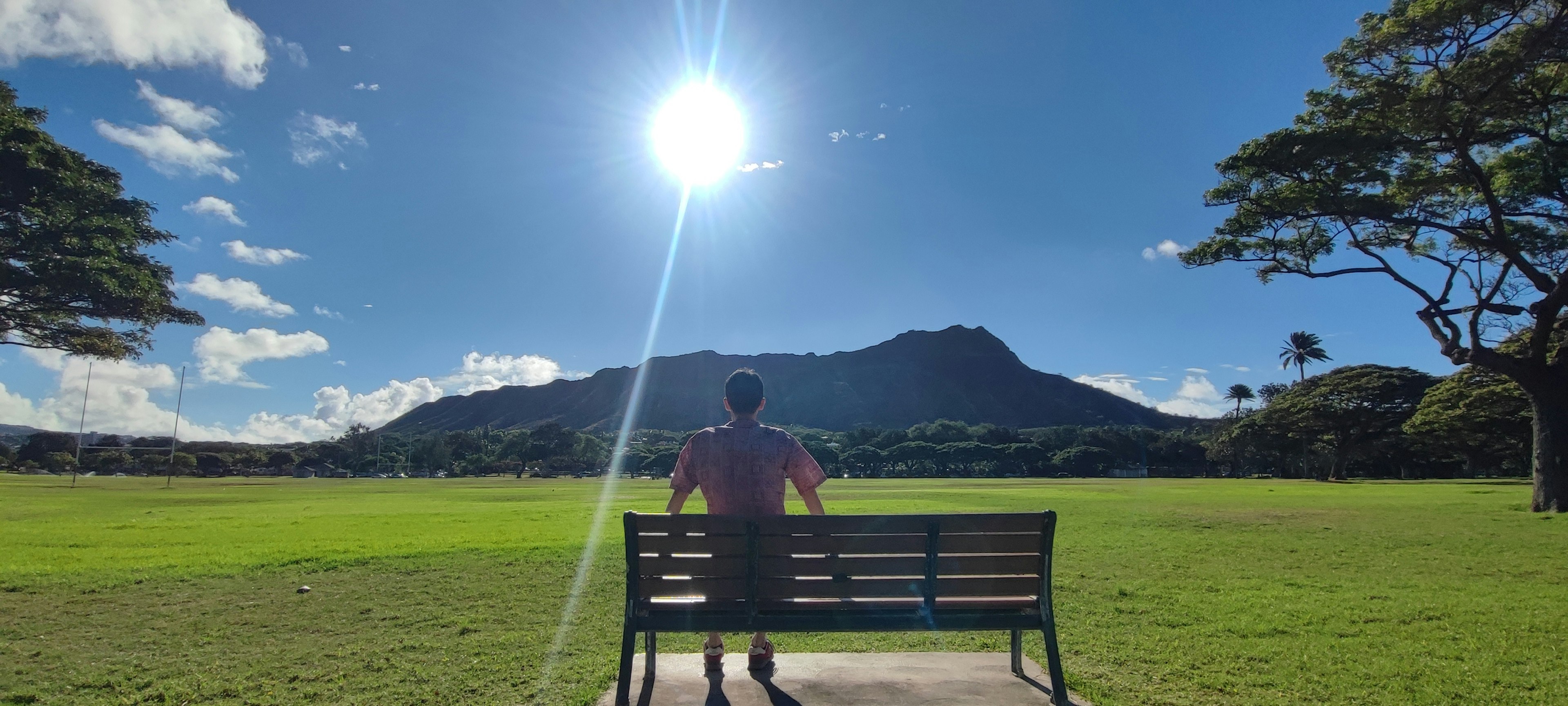 Person sitzt auf einer Parkbank mit majestätischem Berg und blauem Himmel im Hintergrund strahlende Sonne