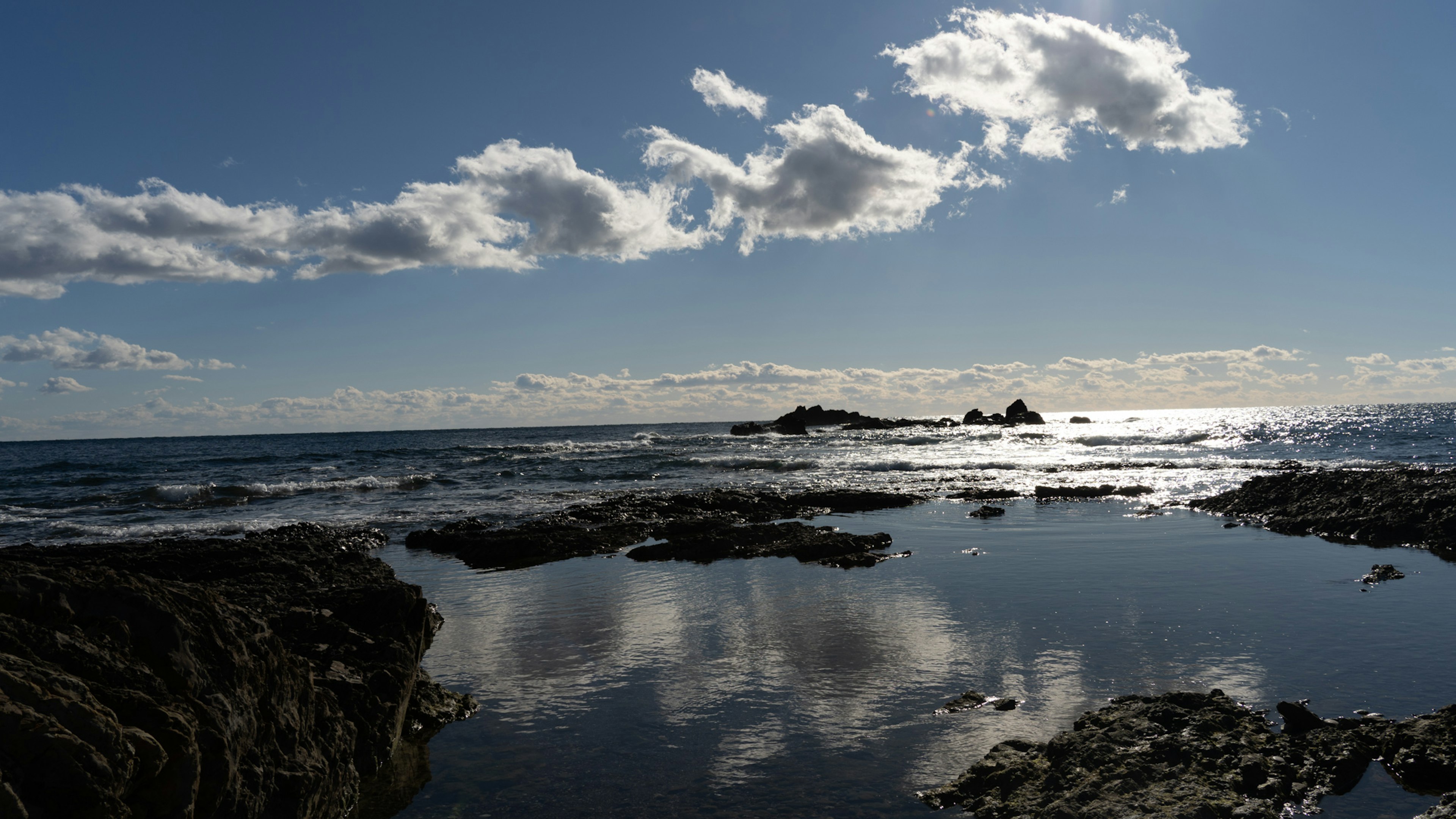 Paesaggio costiero con cielo blu e nuvole bianche che si riflettono nell'acqua calma e costa rocciosa