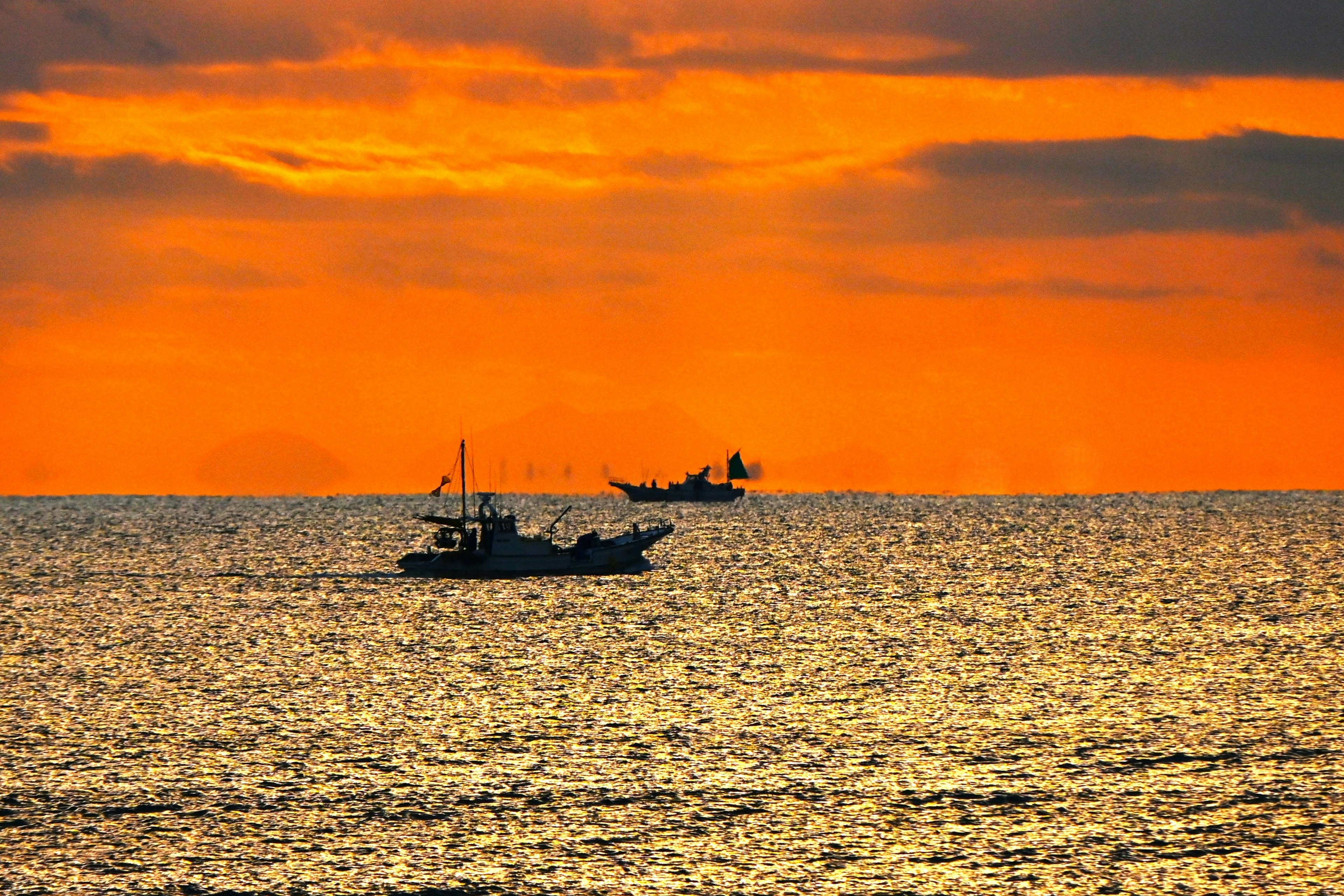 夕日の海に浮かぶ漁船のシルエット