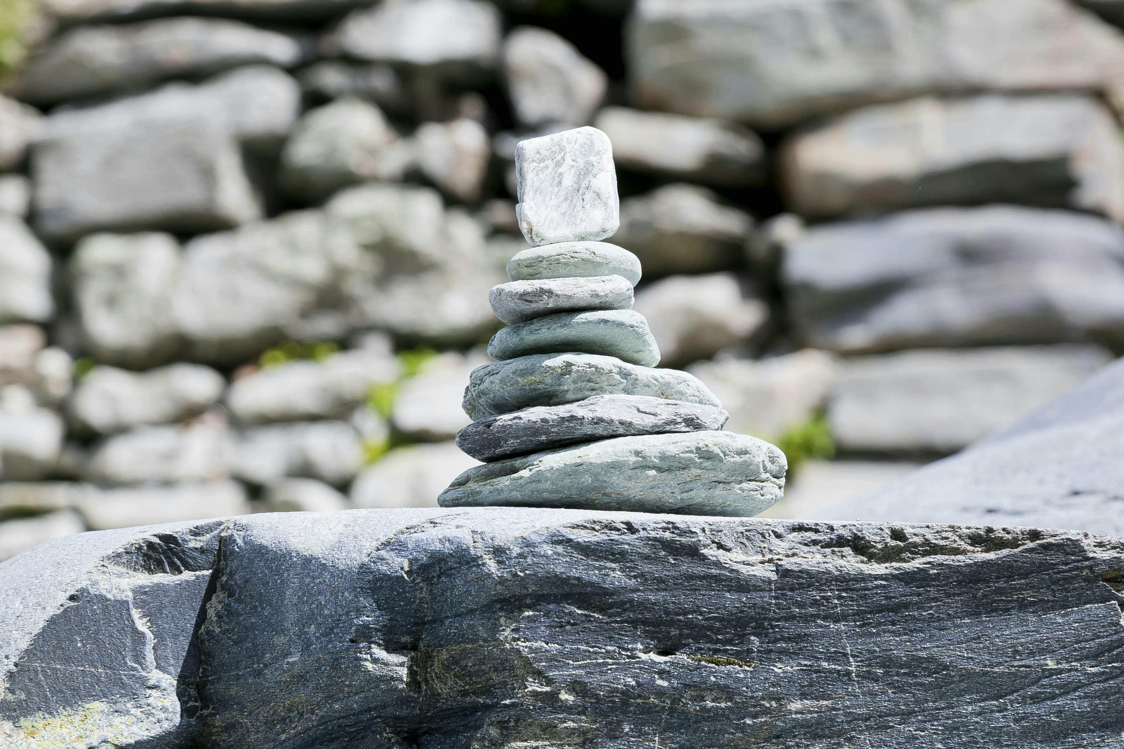 Una torre de piedras equilibrada sobre una roca con un muro de piedras al fondo