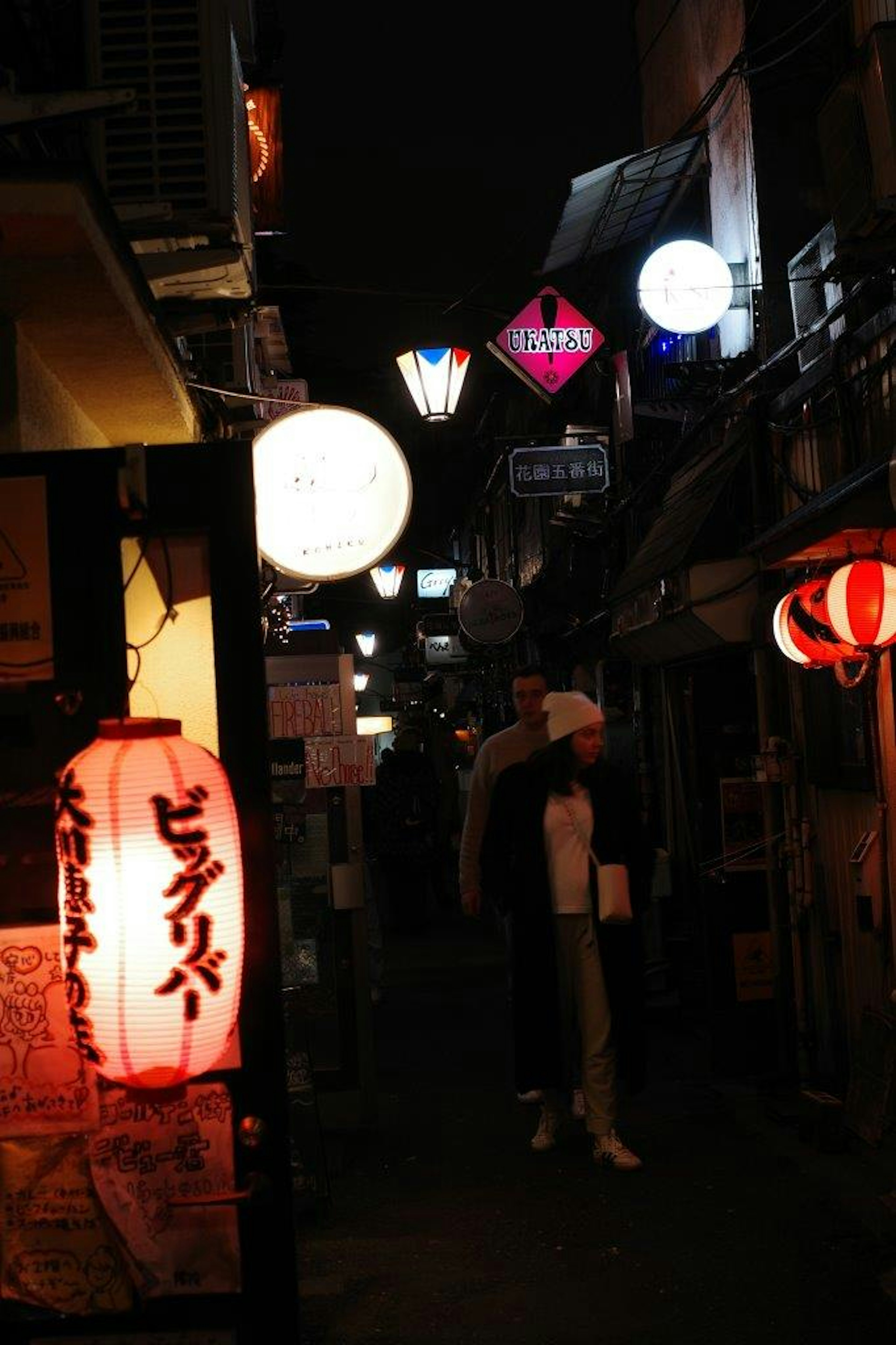 Allée étroite illuminée par des lanternes colorées et des enseignes la nuit