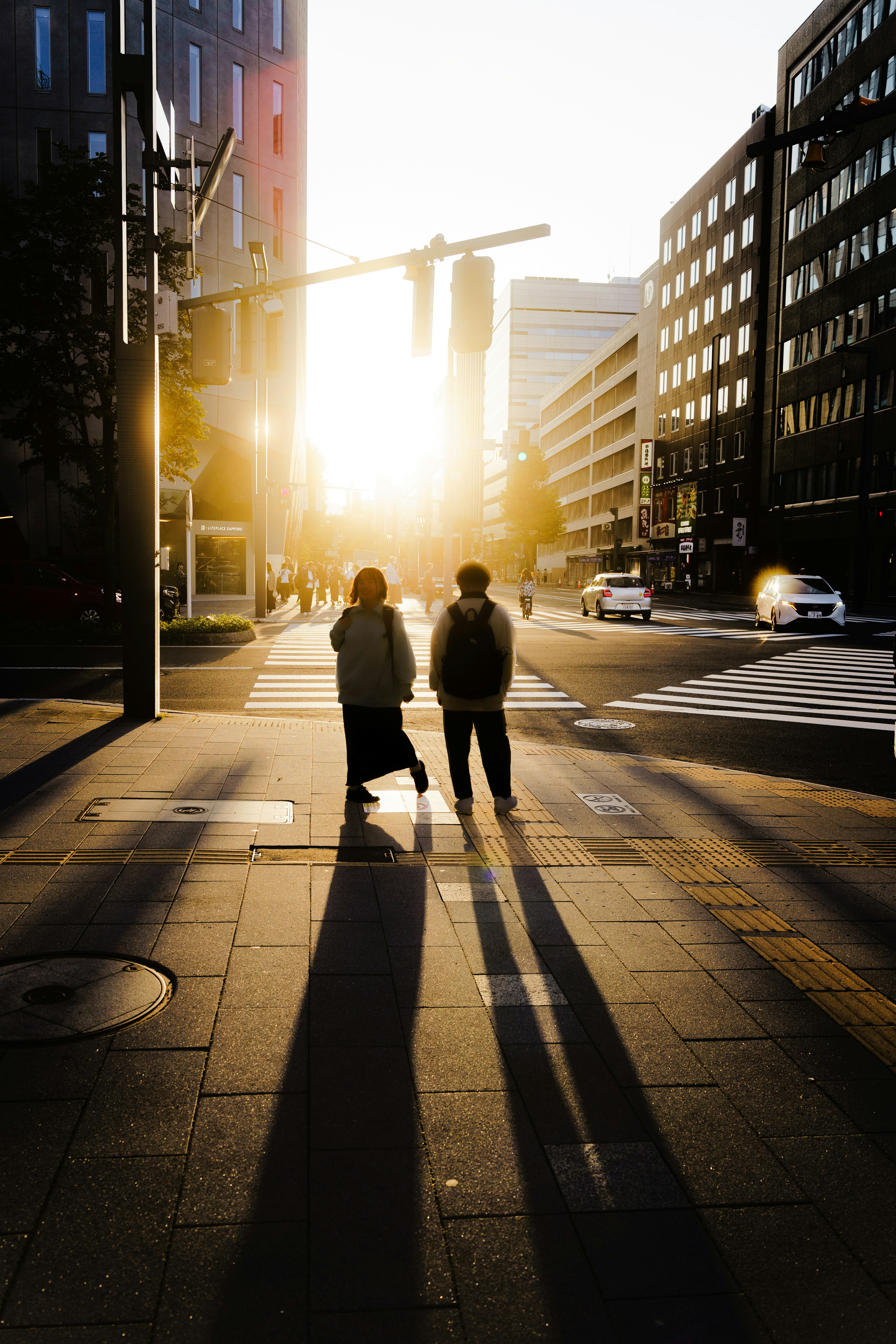 夕日の中を歩く二人の人物と長い影が映る都市の風景