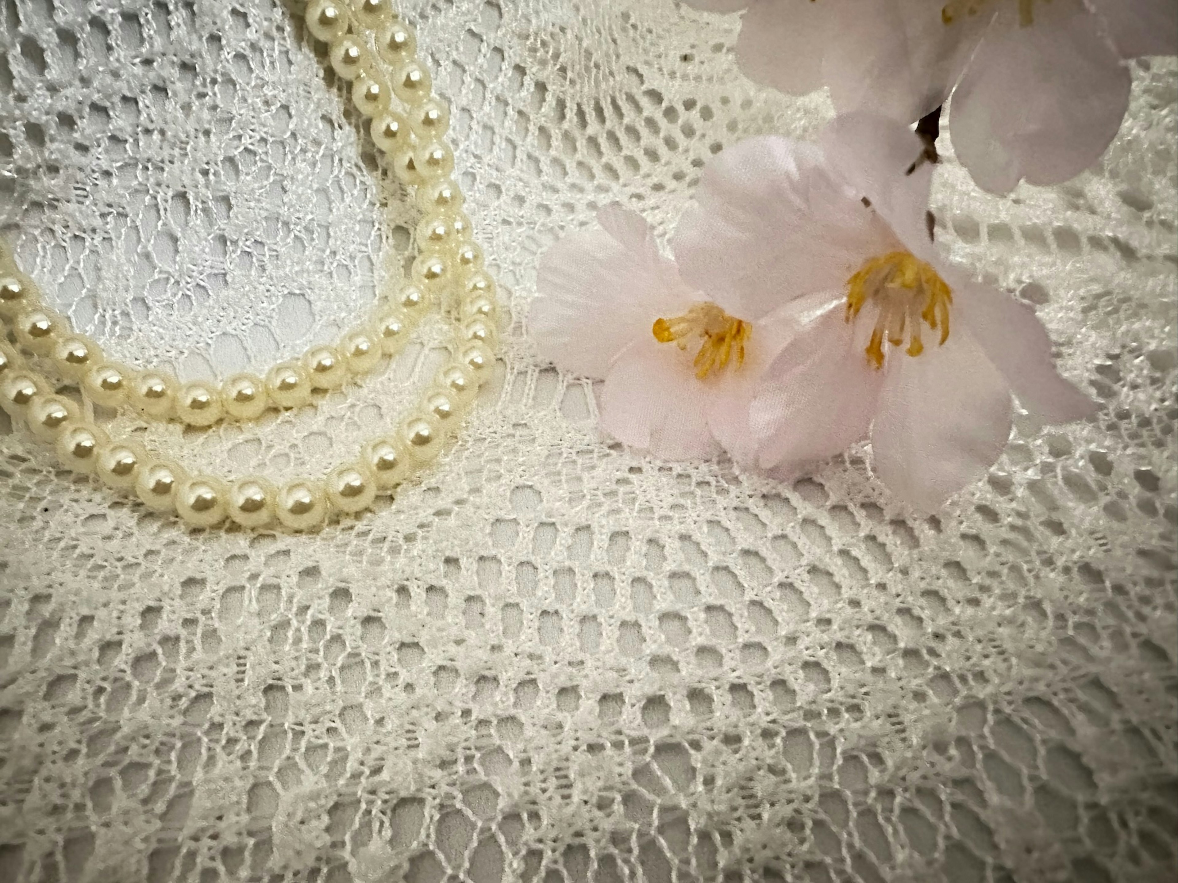 Collana di perle e fiori di ciliegio su sfondo in pizzo bianco