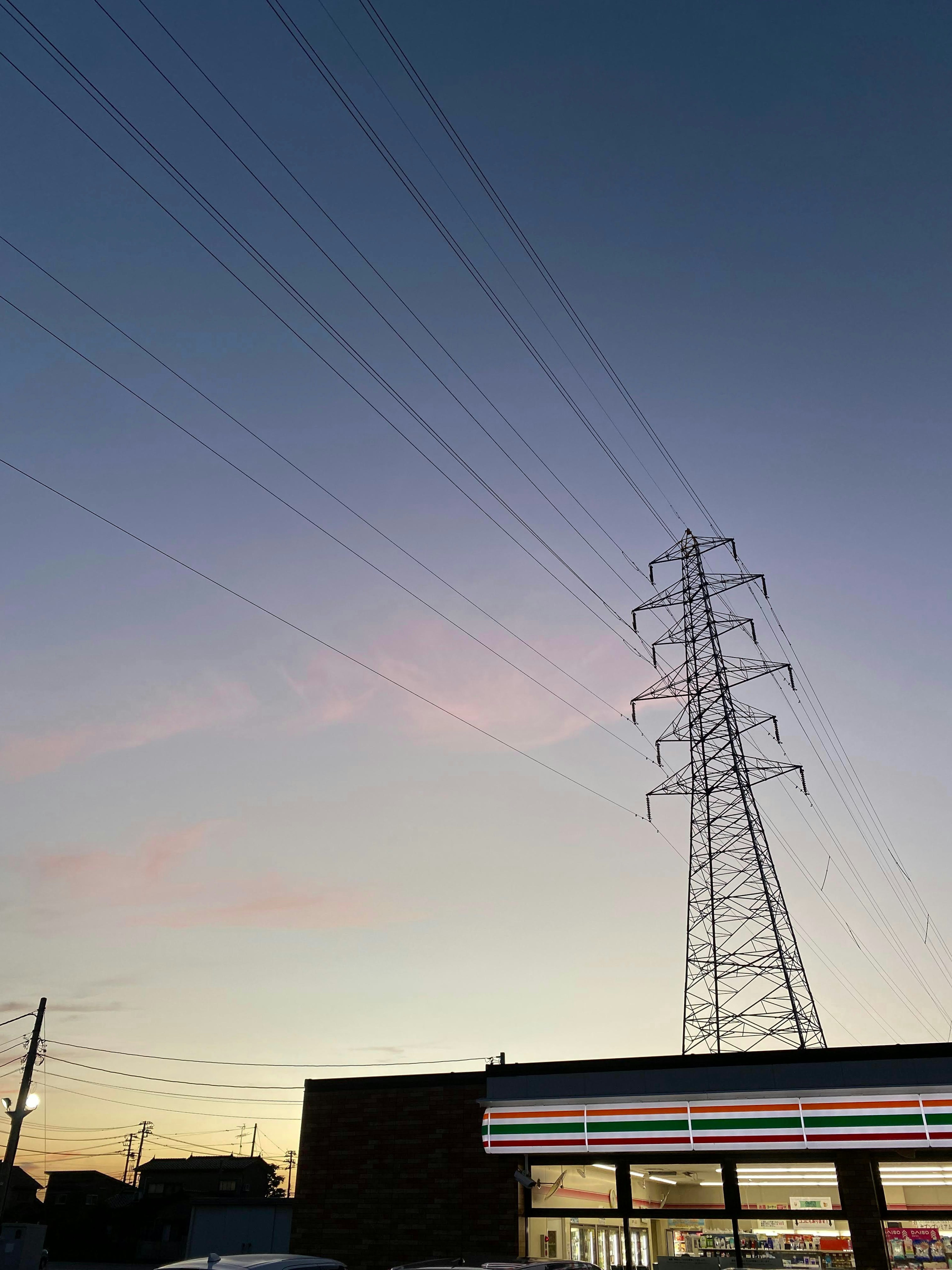 Stromleitungen vor einem bunten Sonnenuntergangshimmel mit einem Geschäft im Vordergrund