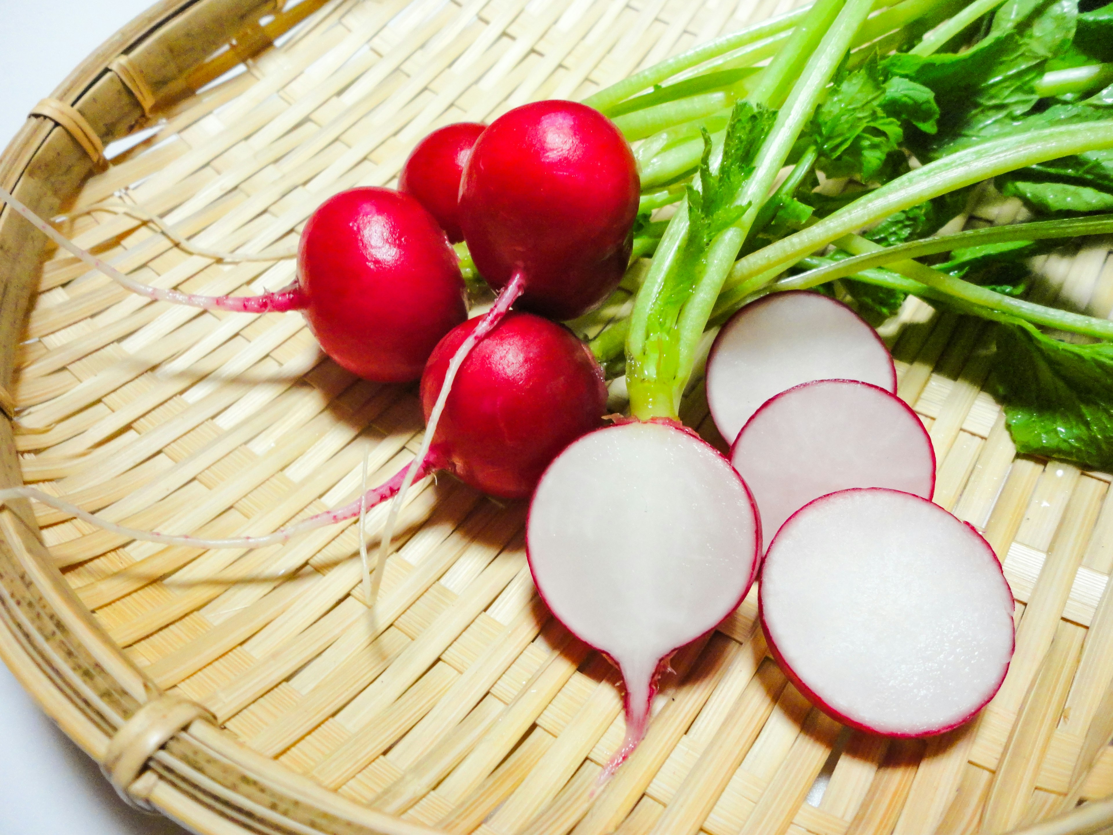 Fresh red radishes and sliced radishes displayed in a bamboo basket