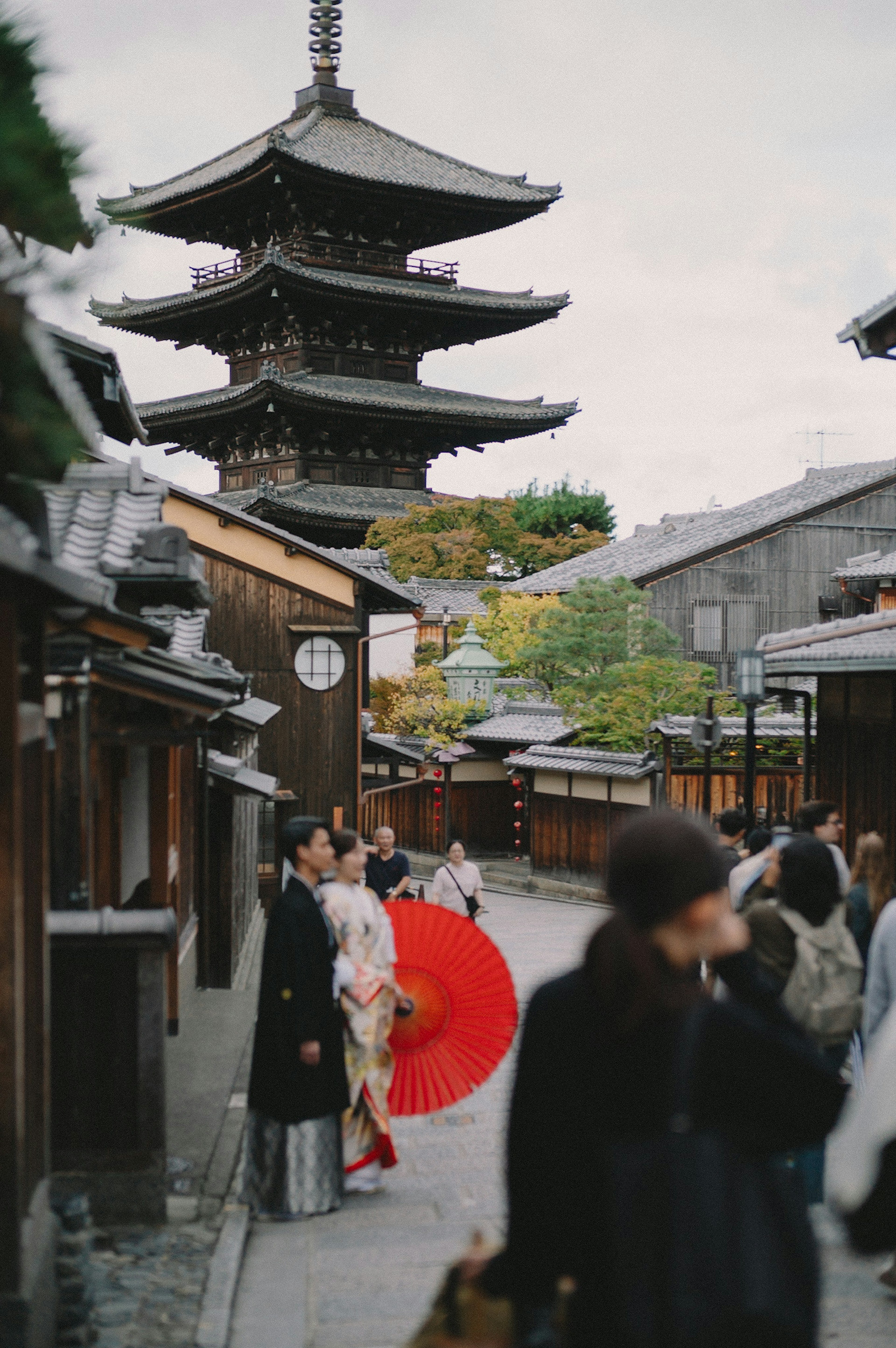 Calle japonesa tradicional con una pagoda al fondo y una mujer sosteniendo un paraguas rojo