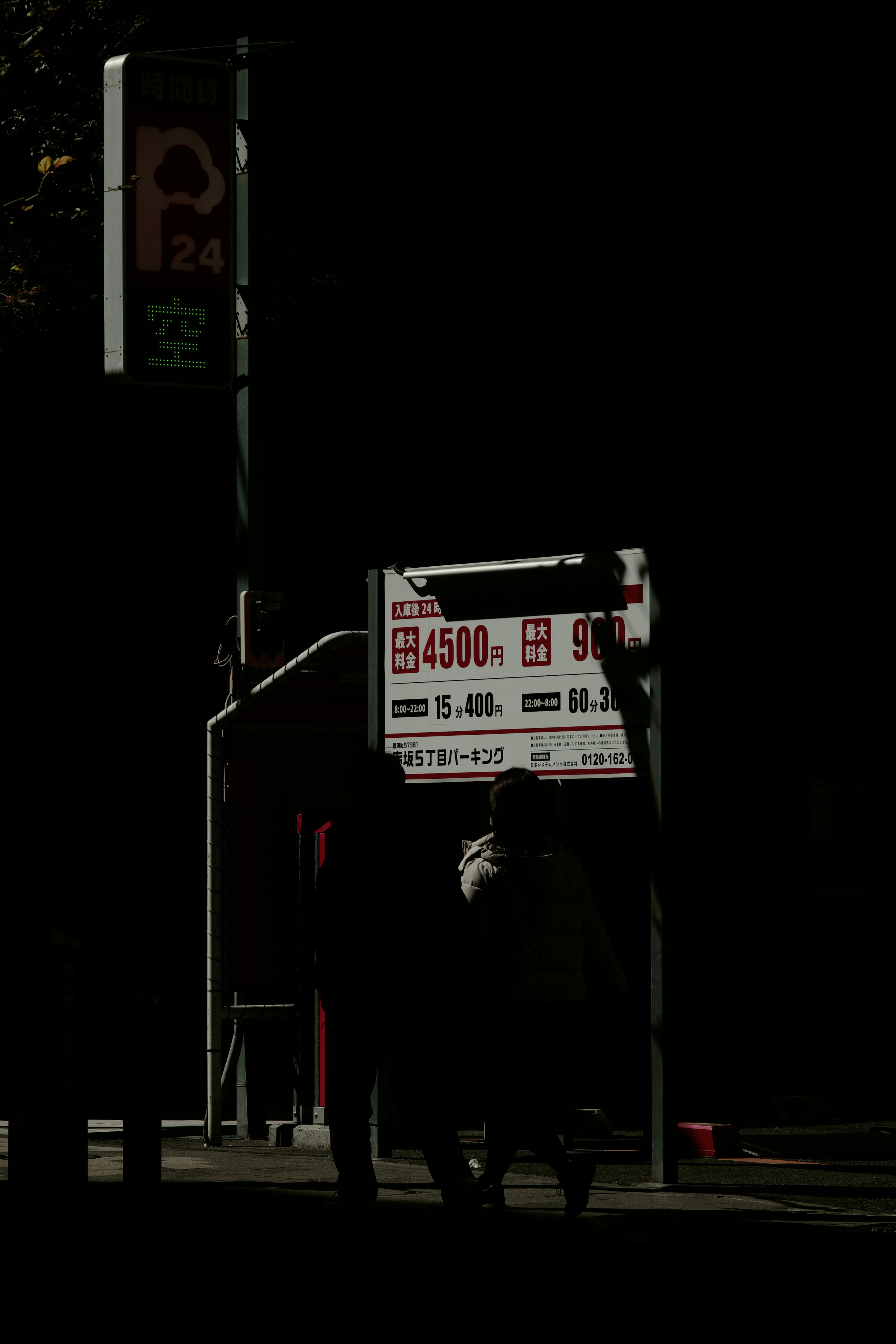 Silhouetted figures walking in a dark street with a sign