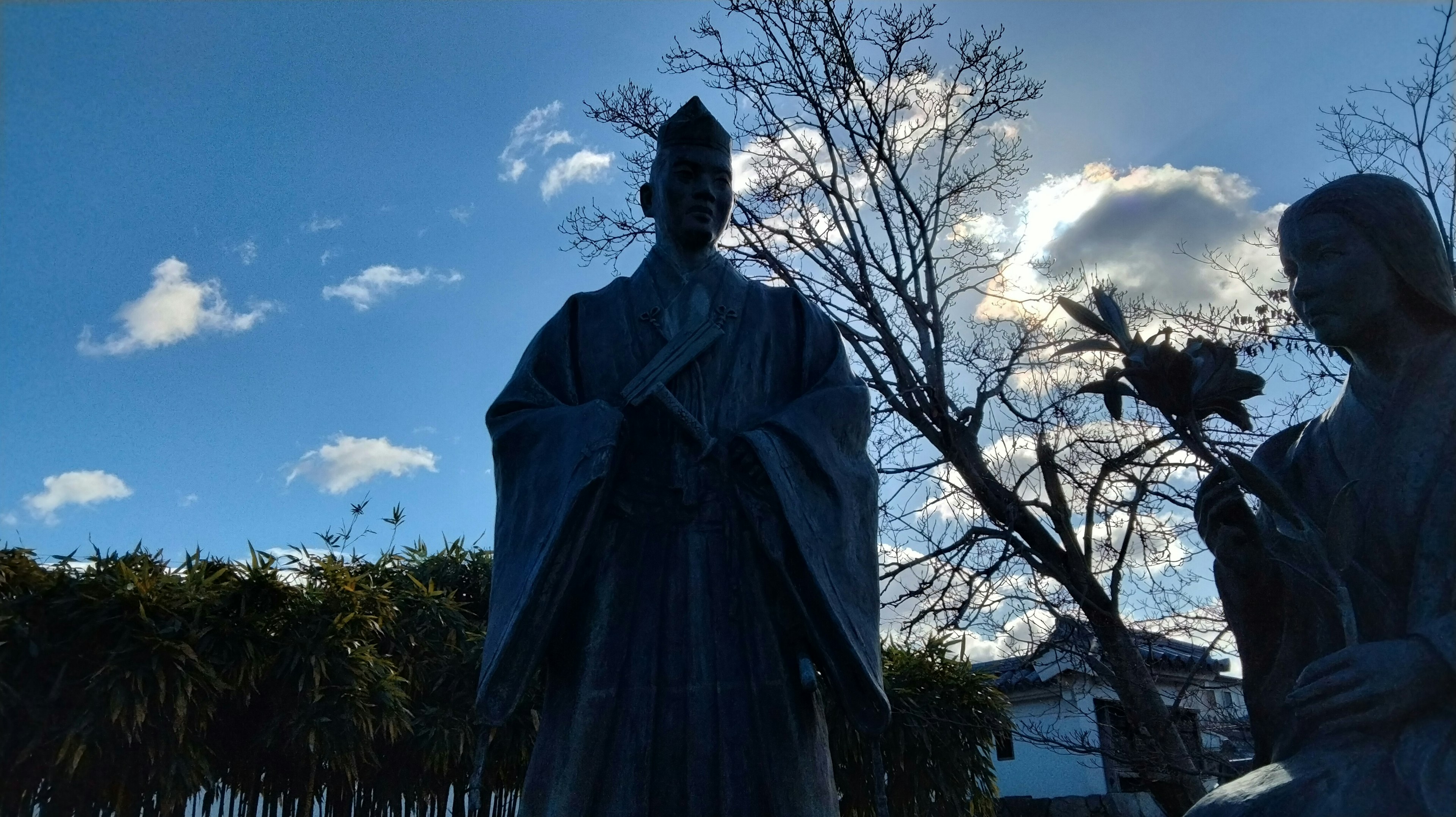 Statue under a blue sky featuring intricate details and surrounding foliage