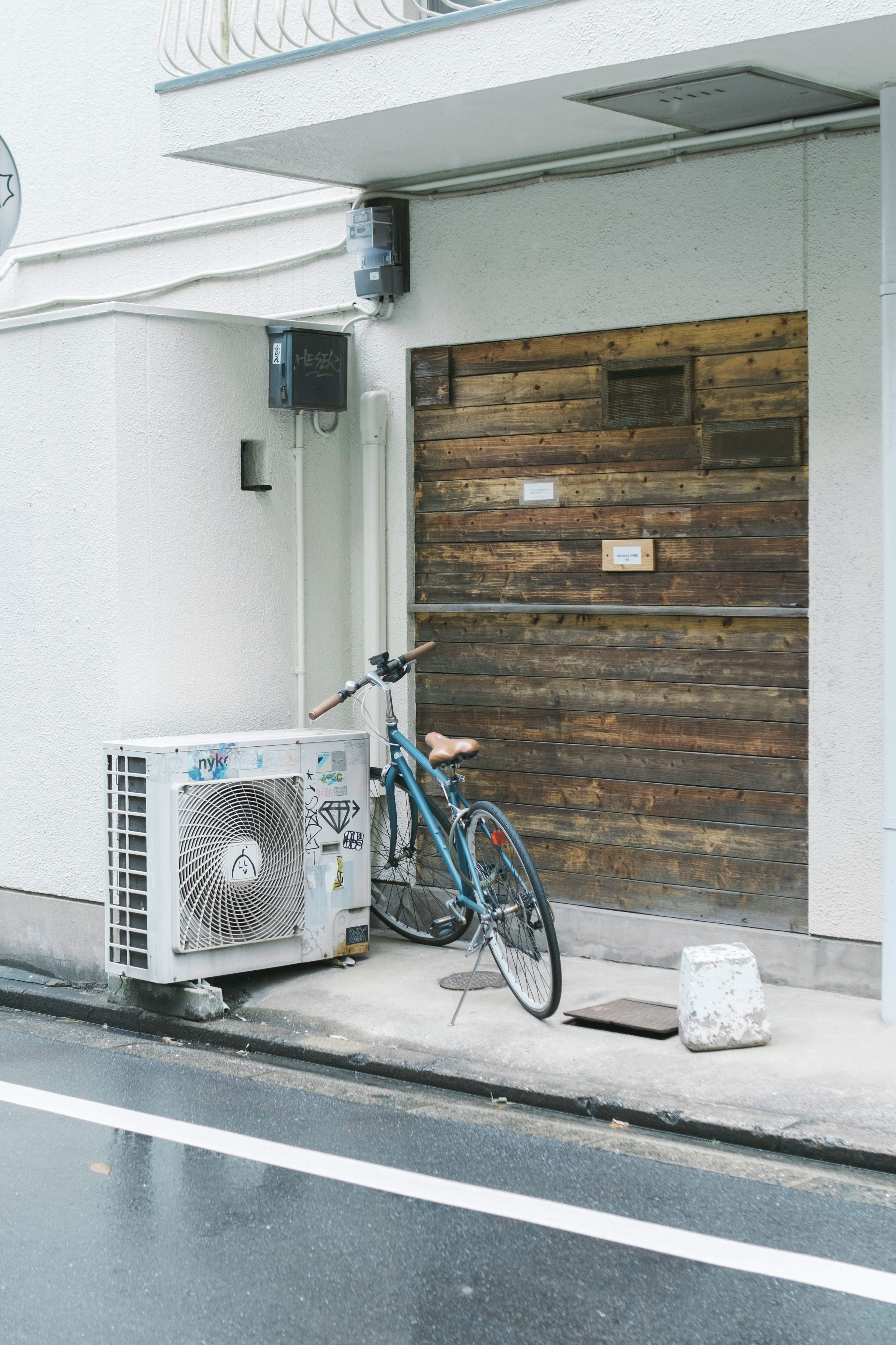 木製のドアの前に置かれた青い自転車とエアコンの室外機