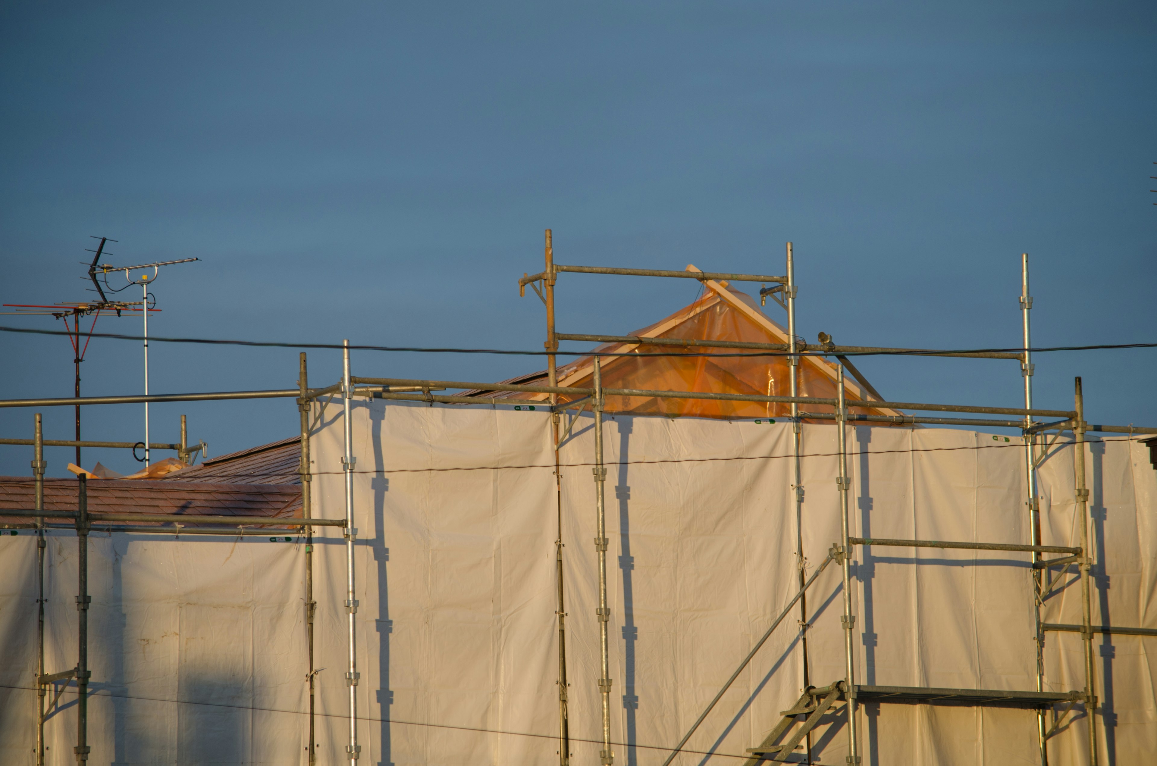 Andamio y lona blanca cubriendo una casa en construcción con un techo visible