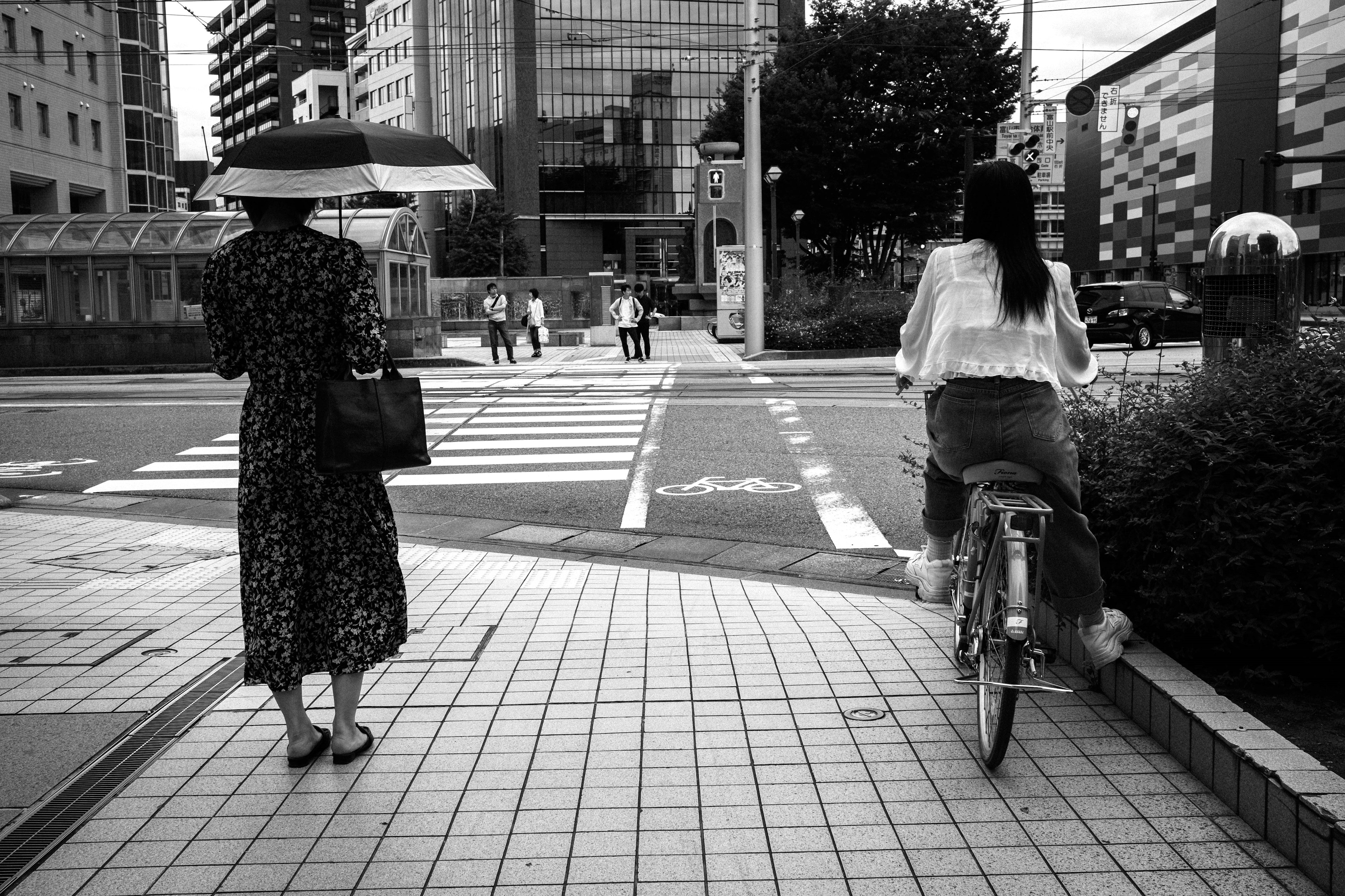 Une femme marchant avec un parapluie à côté d'une autre femme faisant du vélo dans un environnement urbain