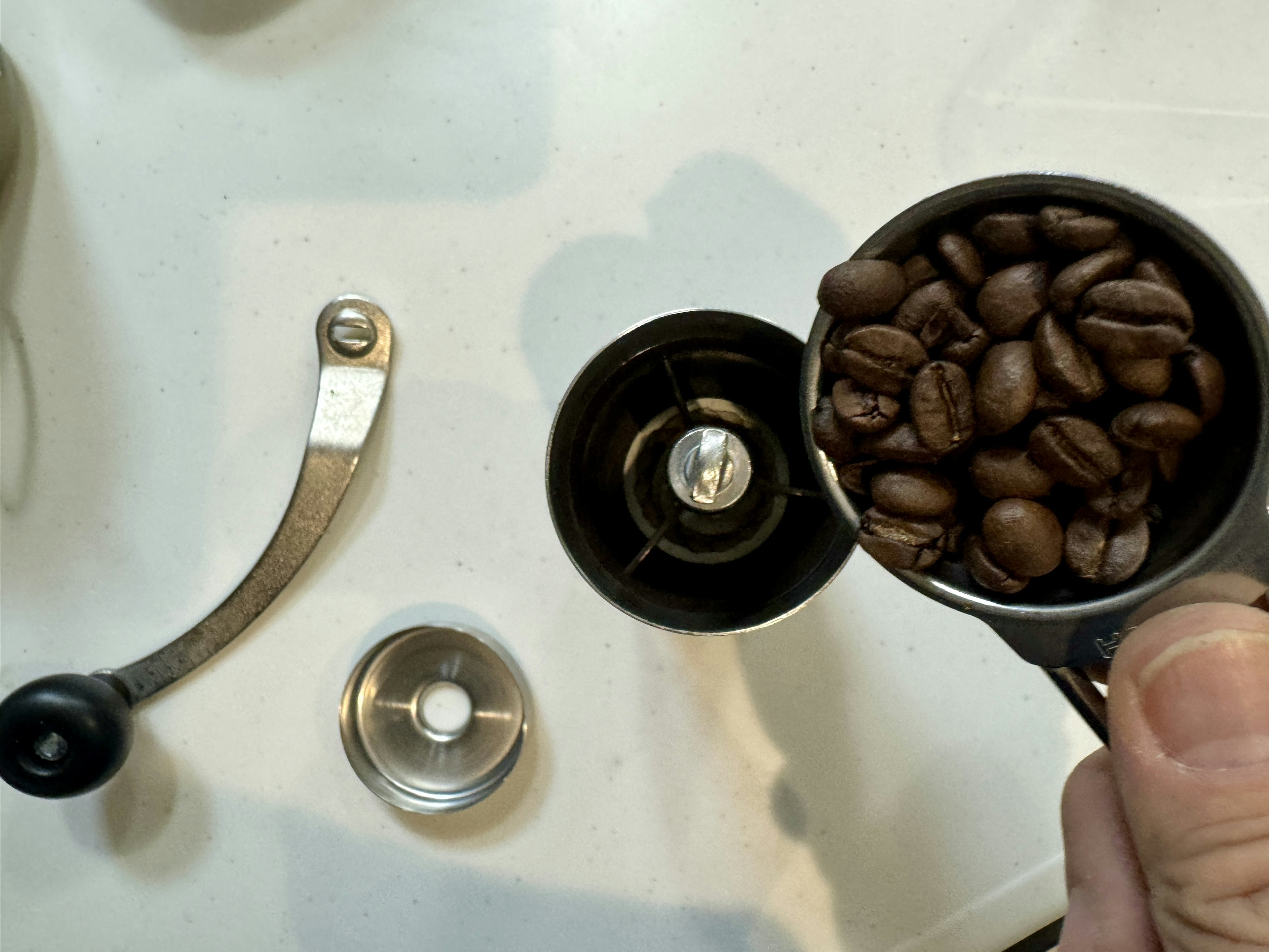 Coffee beans in a measuring cup above a coffee grinder with tools nearby