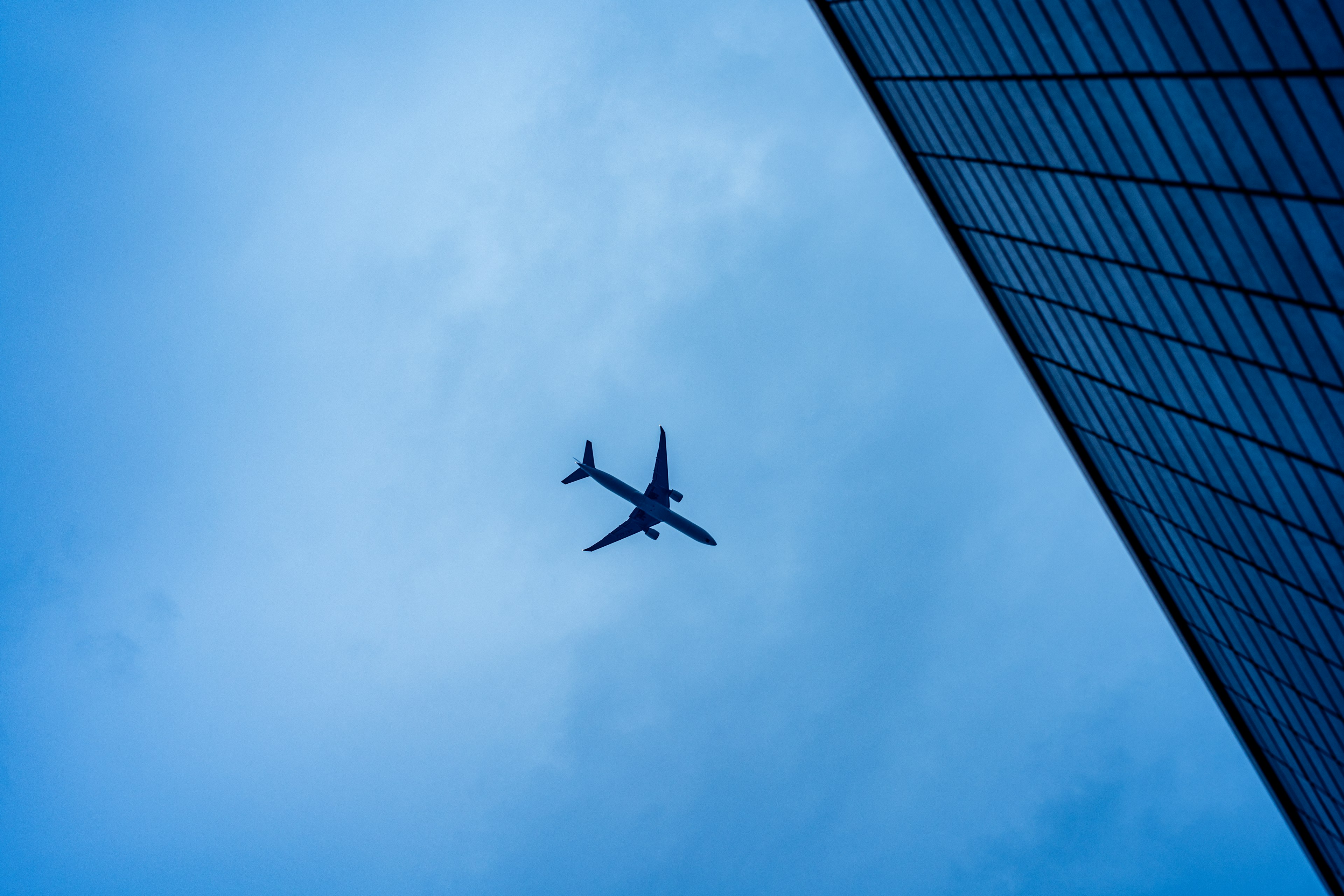 Airplane flying against a blue sky with a building edge