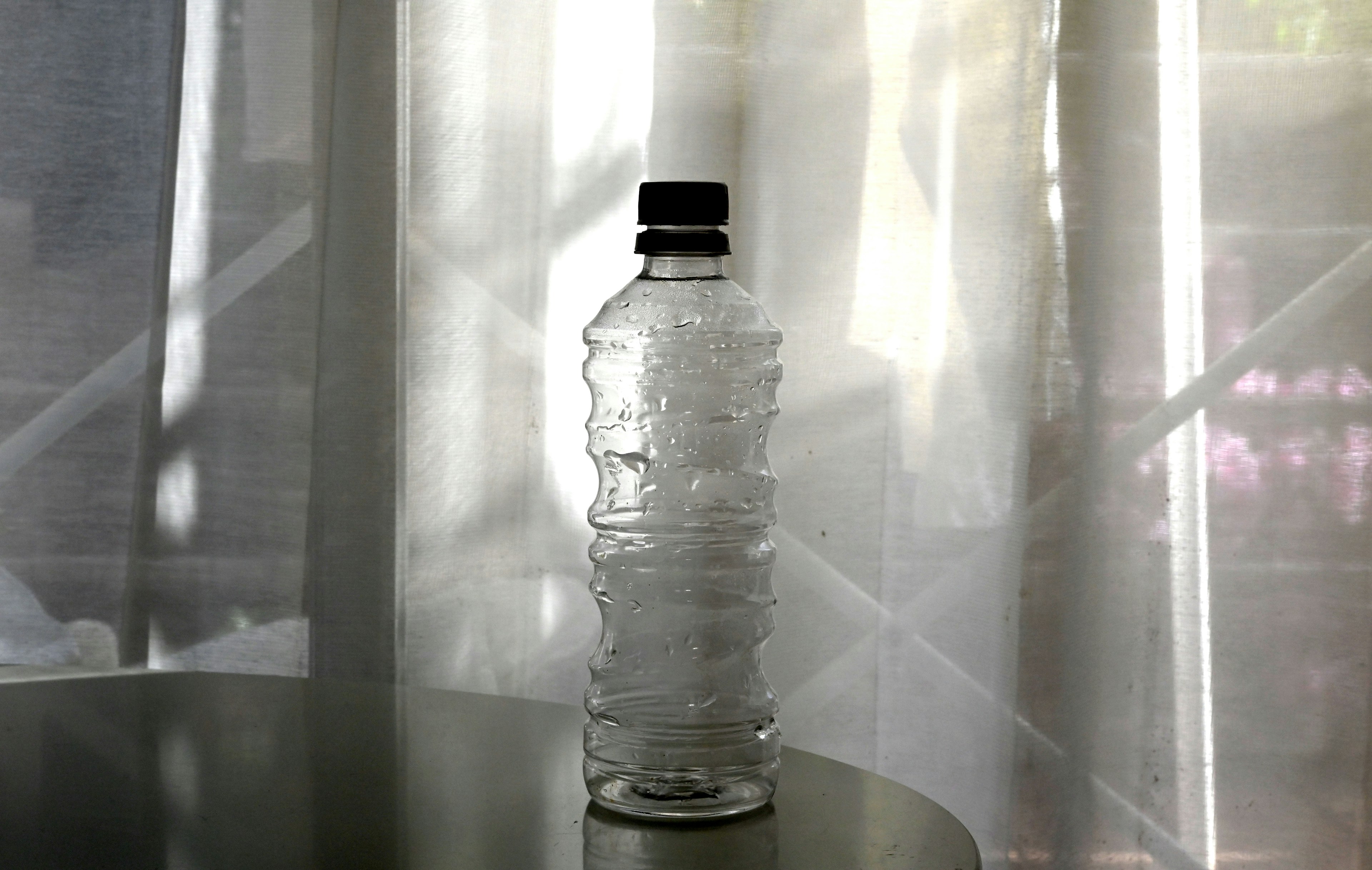 A clear water bottle placed in front of white curtains