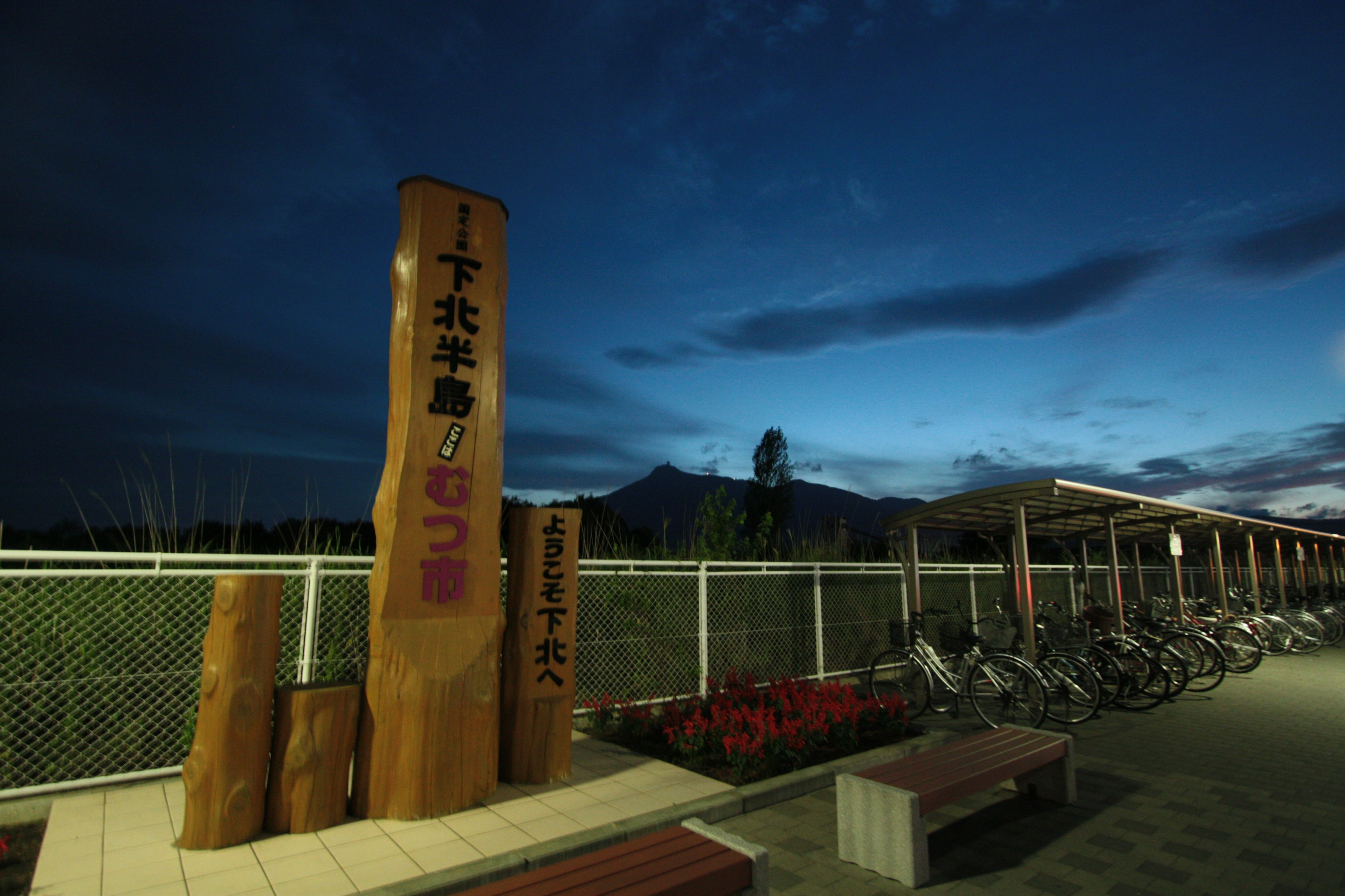 Gran cartel de madera bajo el cielo nocturno con área de estacionamiento para bicicletas