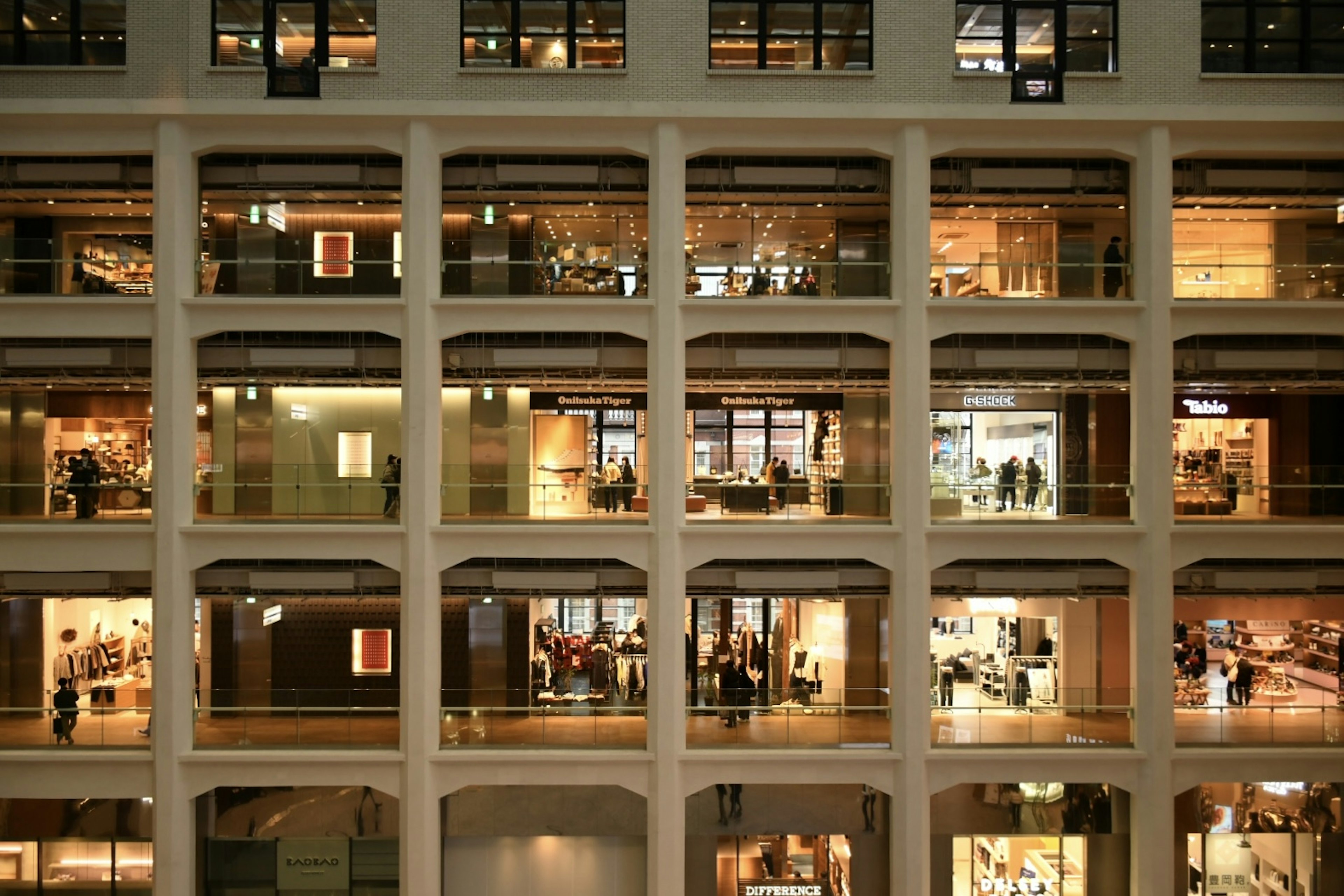 Fachada de un edificio comercial brillante con múltiples ventanas que muestran tiendas y personas adentro