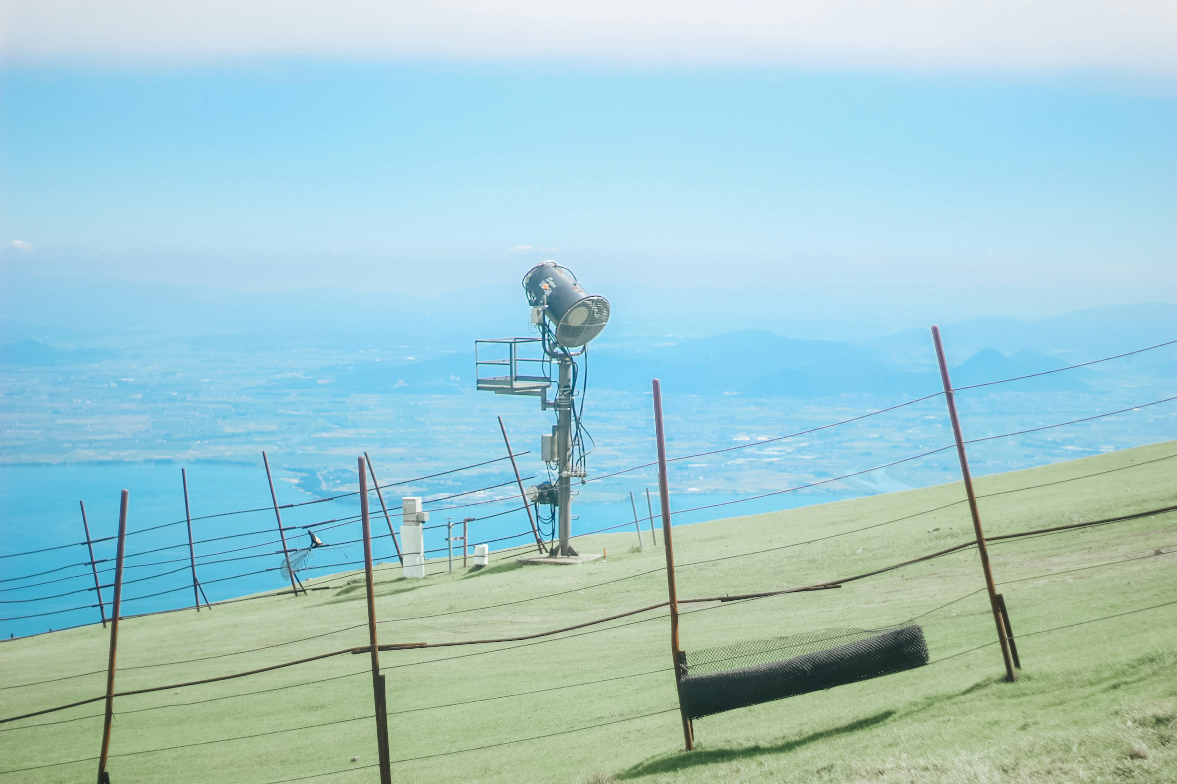 Communication tower on a grassy hillside with a distant view