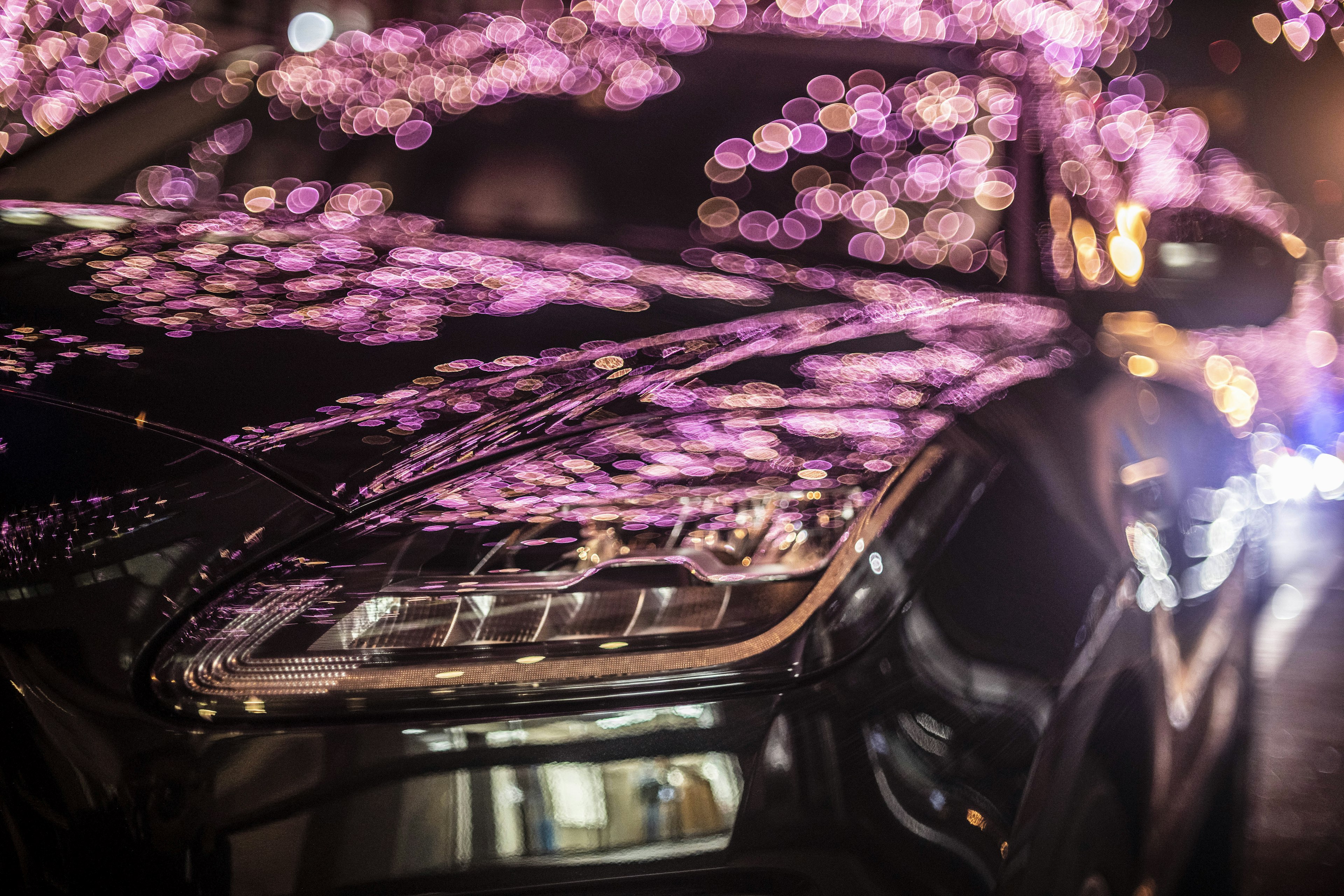 Nahaufnahme eines schwarzen Autos, das violette Bokehlichter in der Nacht reflektiert