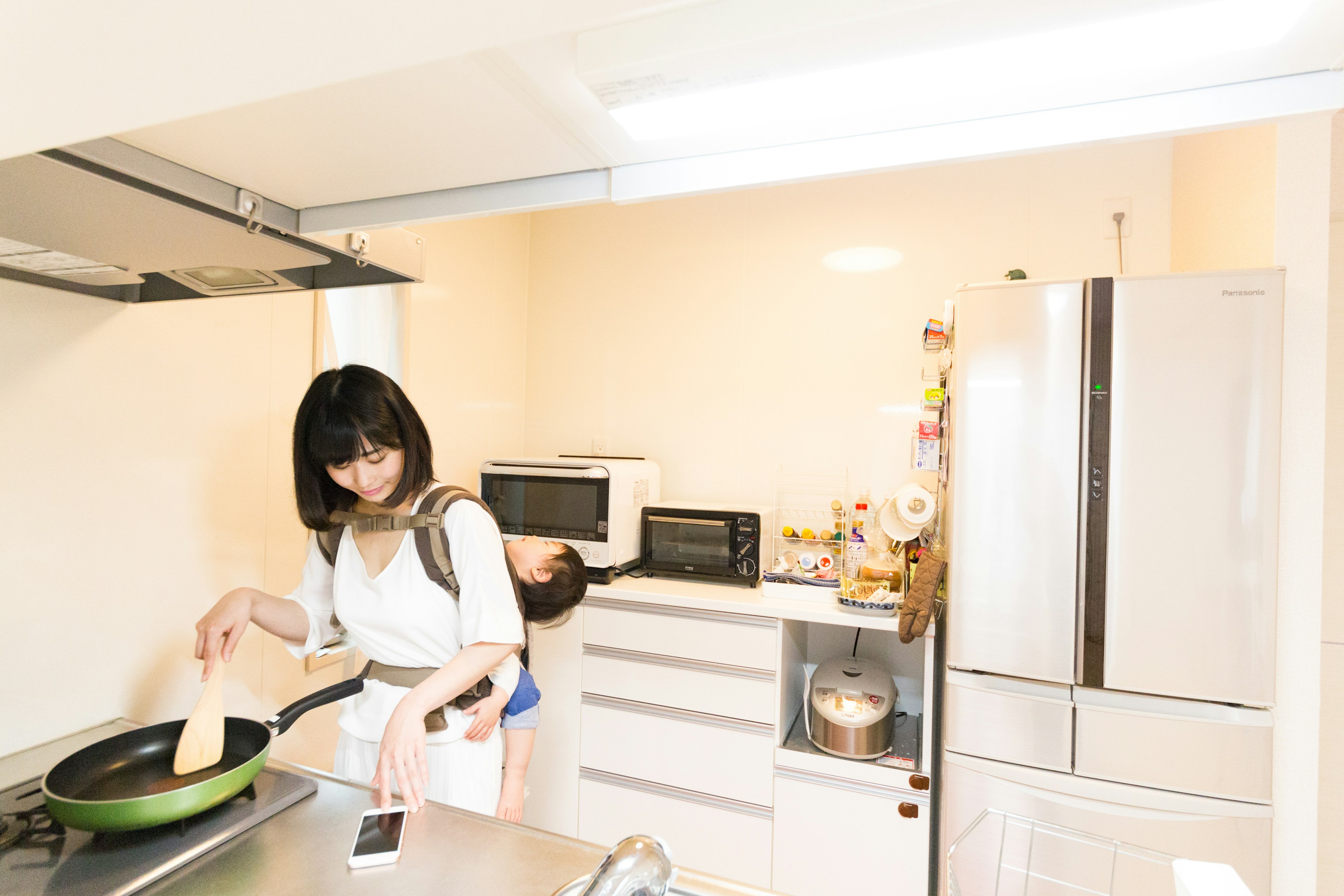 Une femme cuisinant dans une cuisine avec une poêle et un réfrigérateur visibles