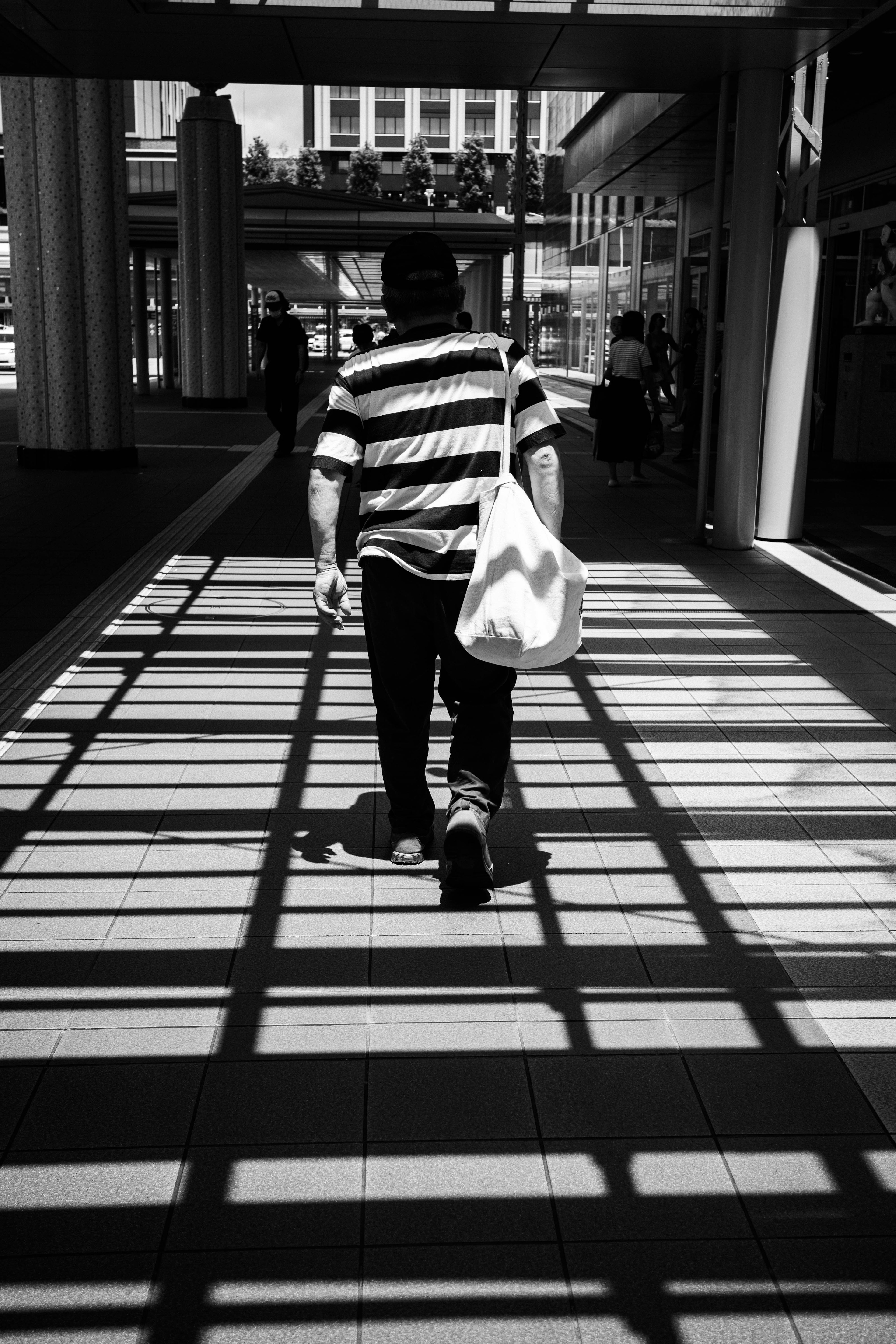 A person in a black and white striped shirt walking with a bag Shadows cast on the floor