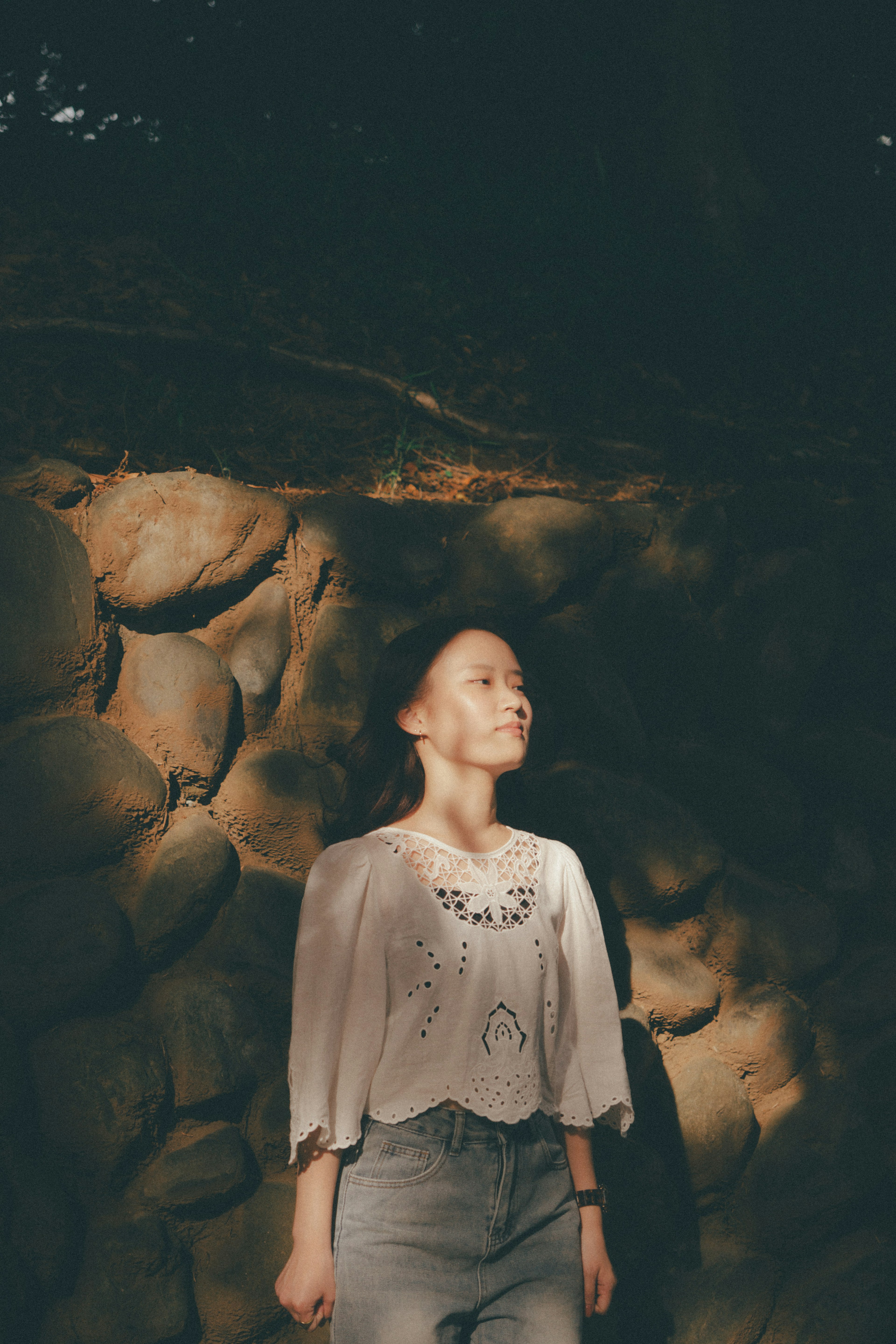 Retrato de una mujer de pie en suave luz natural frente a un muro de piedra