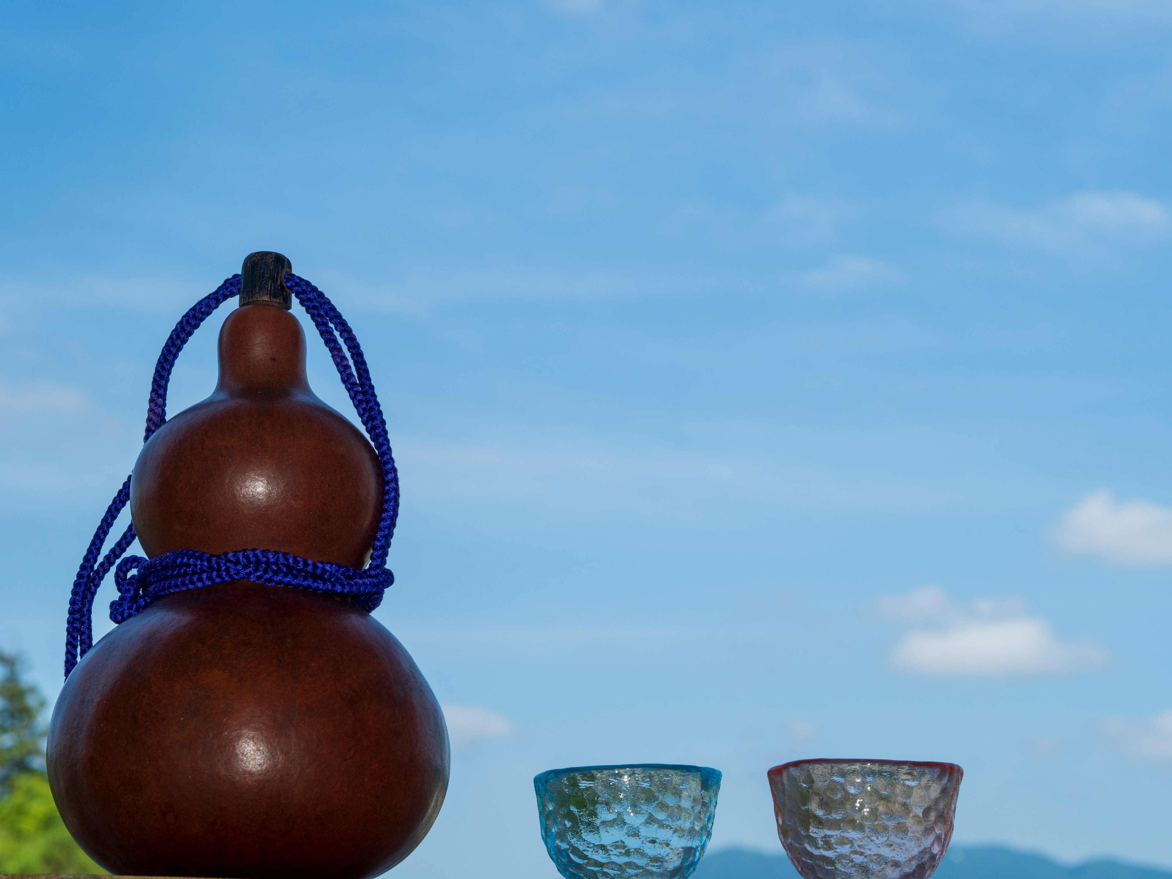 Brown gourd with blue cord beside two clear glasses under blue sky