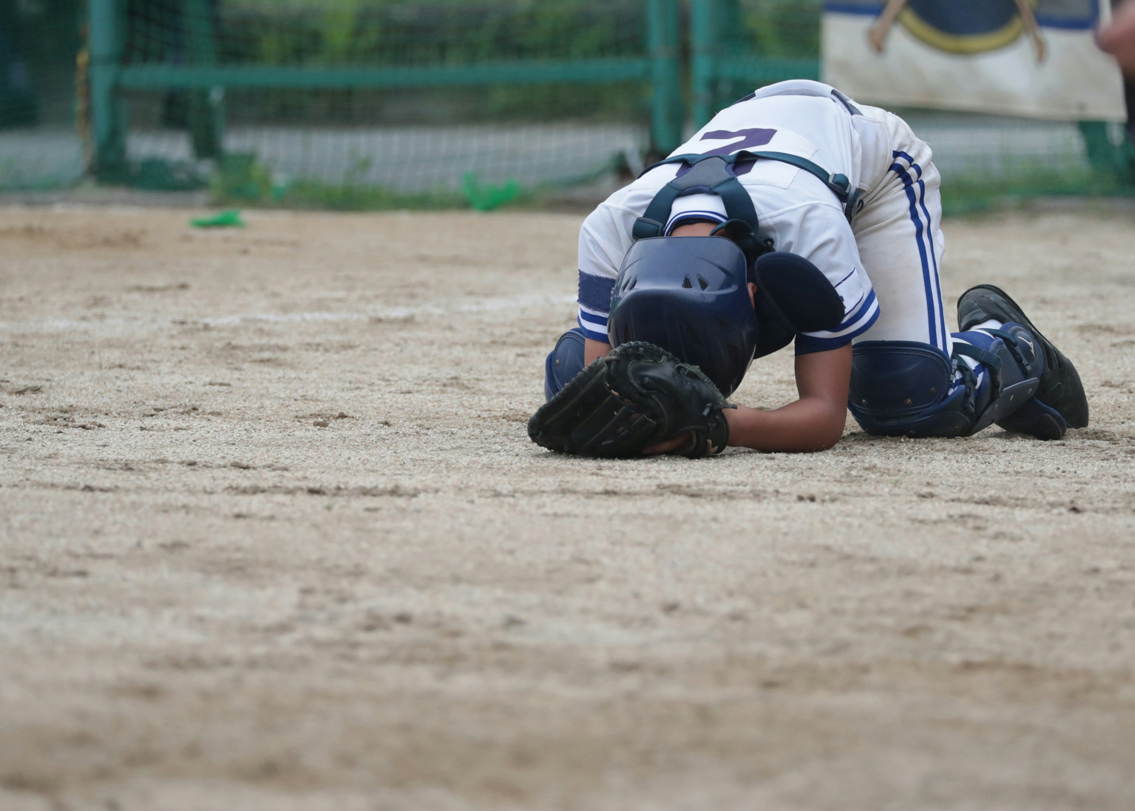 A baseball player kneeling on the ground with their head down