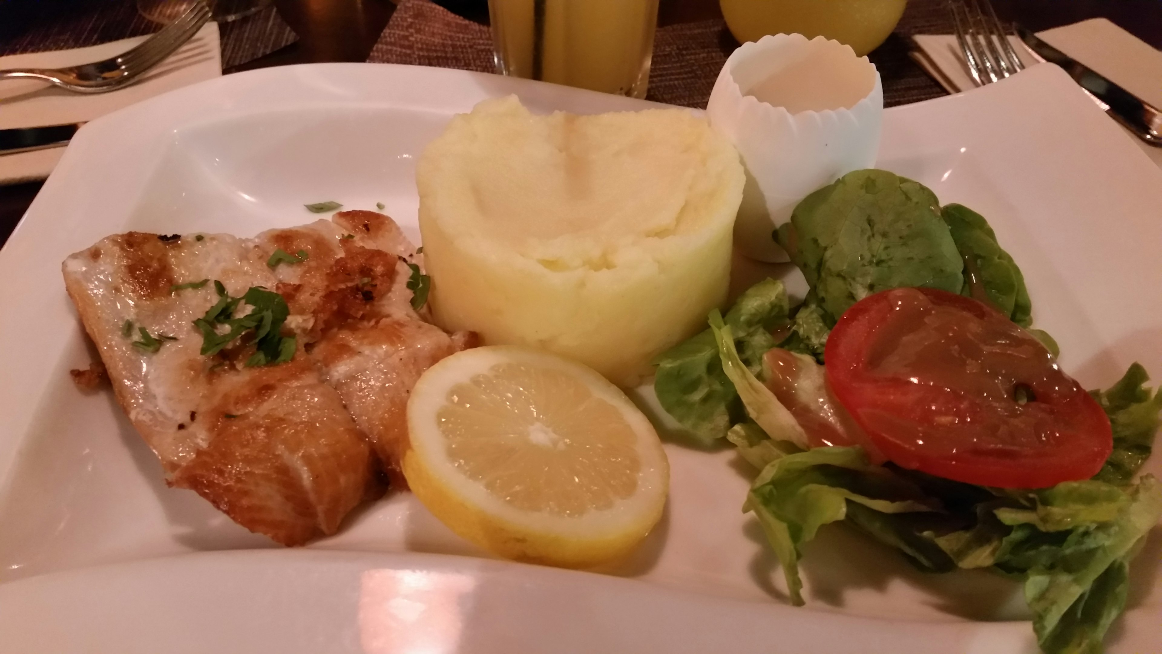 Pesce alla griglia servito su un piatto bianco con purè di patate insalata fresca e fette di limone