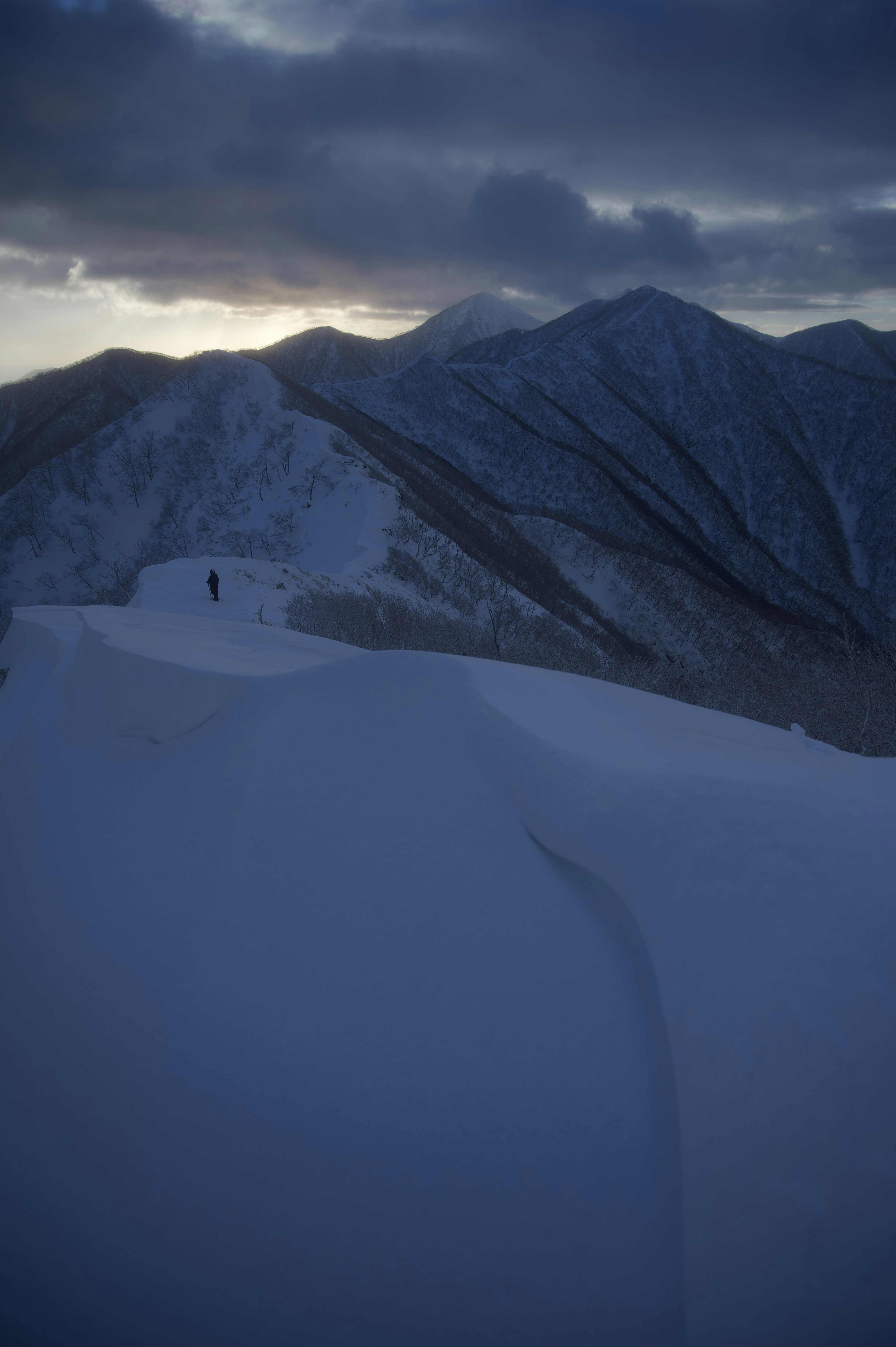 Paisaje montañoso cubierto de nieve con un excursionista solitario a lo lejos