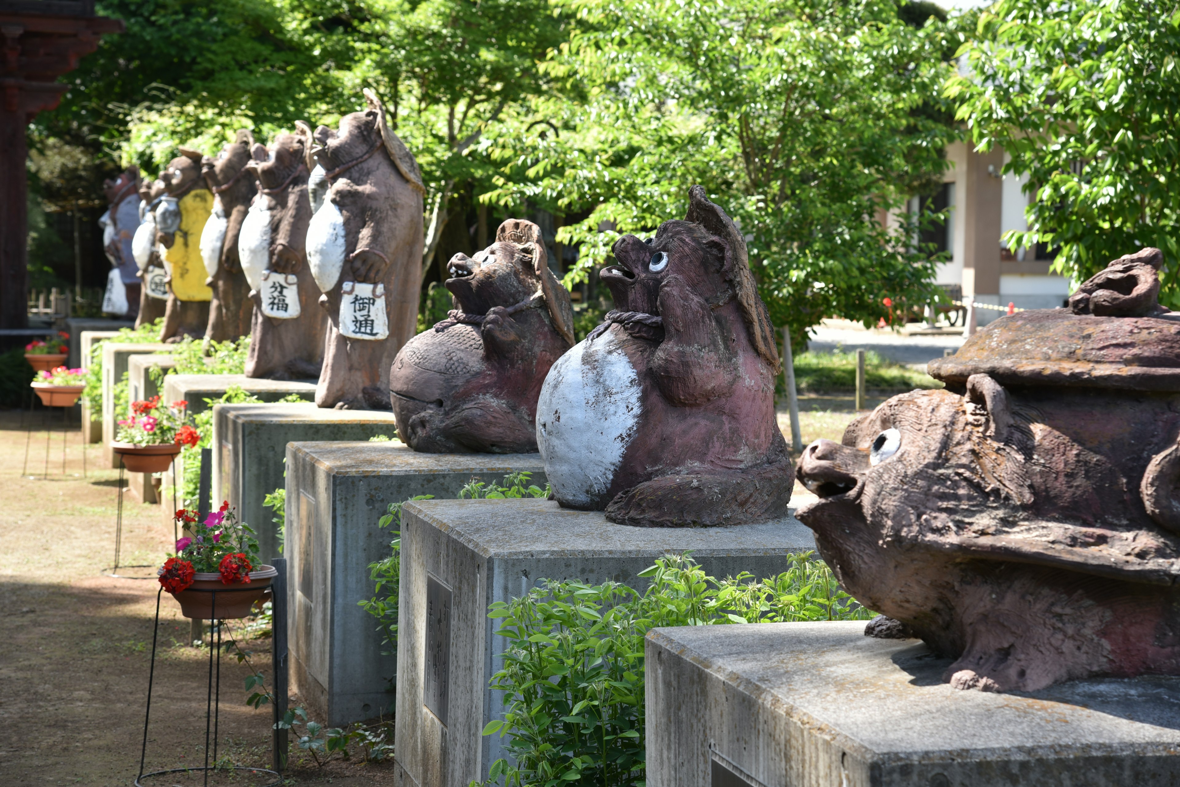 A row of ceramic tanuki sculptures in a garden surrounded by green trees