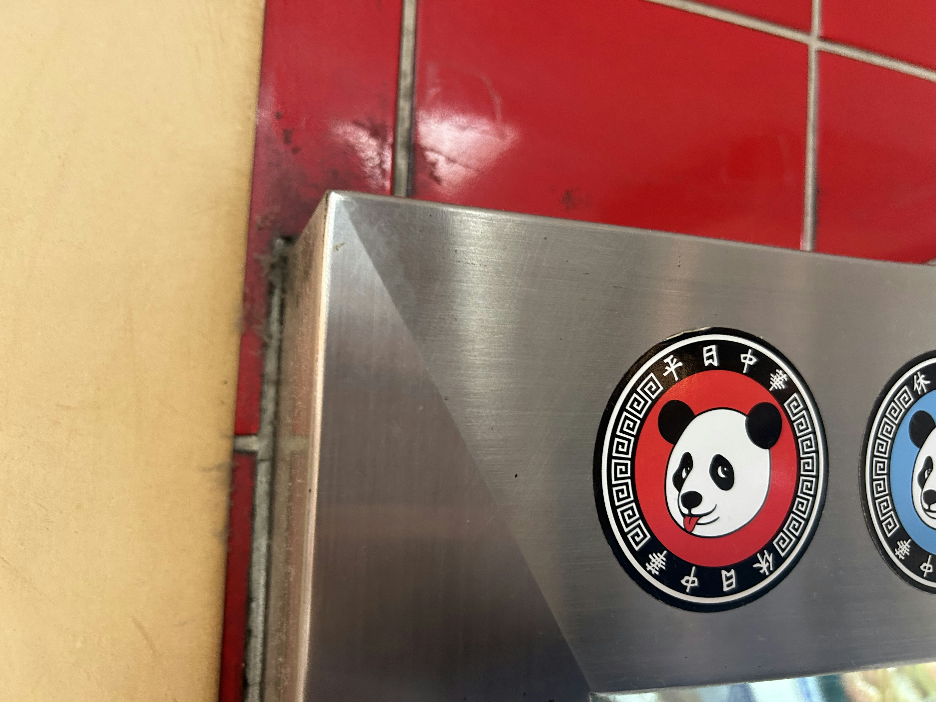 Red tiled wall with stainless steel panel featuring panda logo stickers