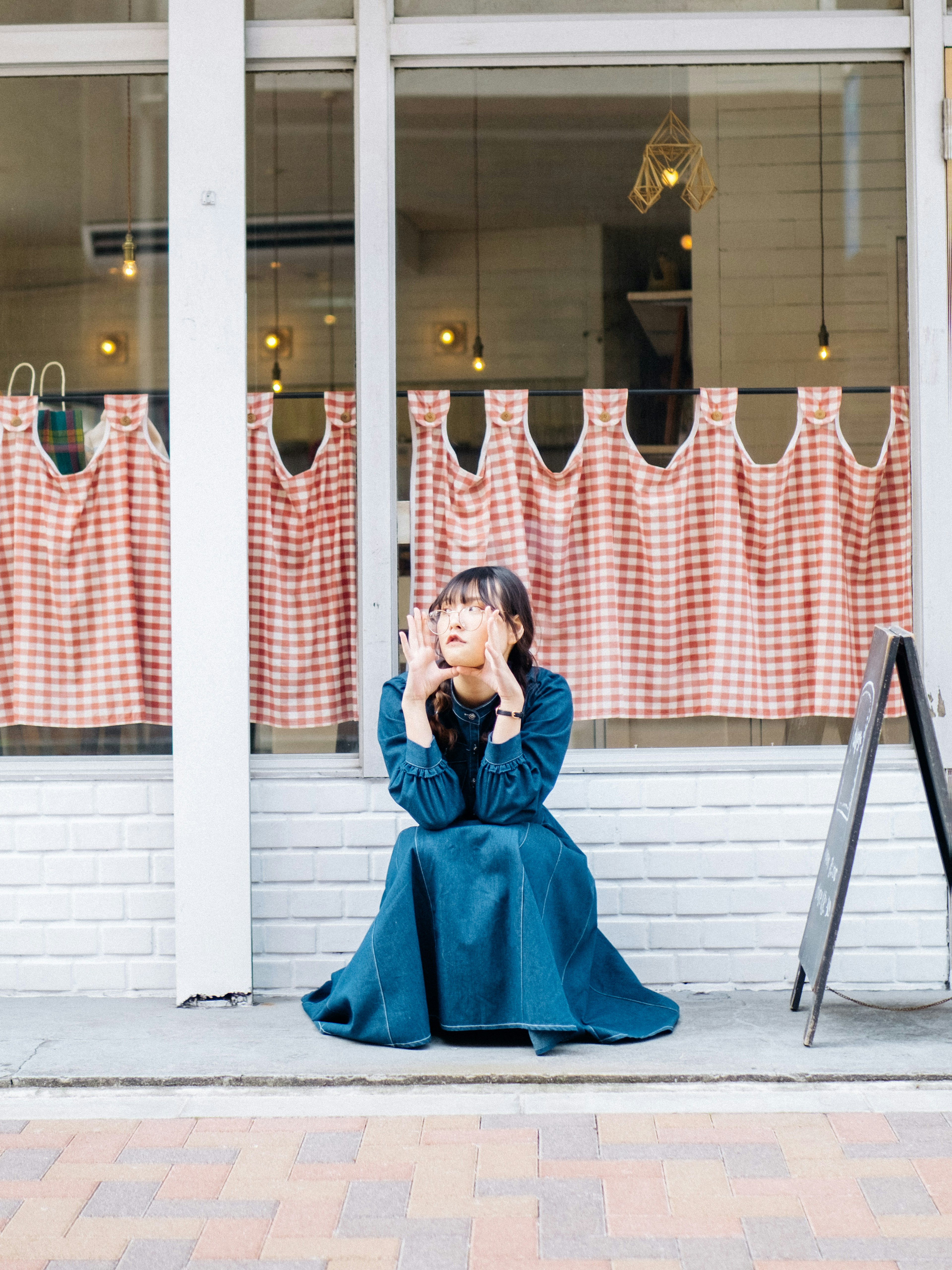 A woman in a blue dress sitting in front of red checkered curtains