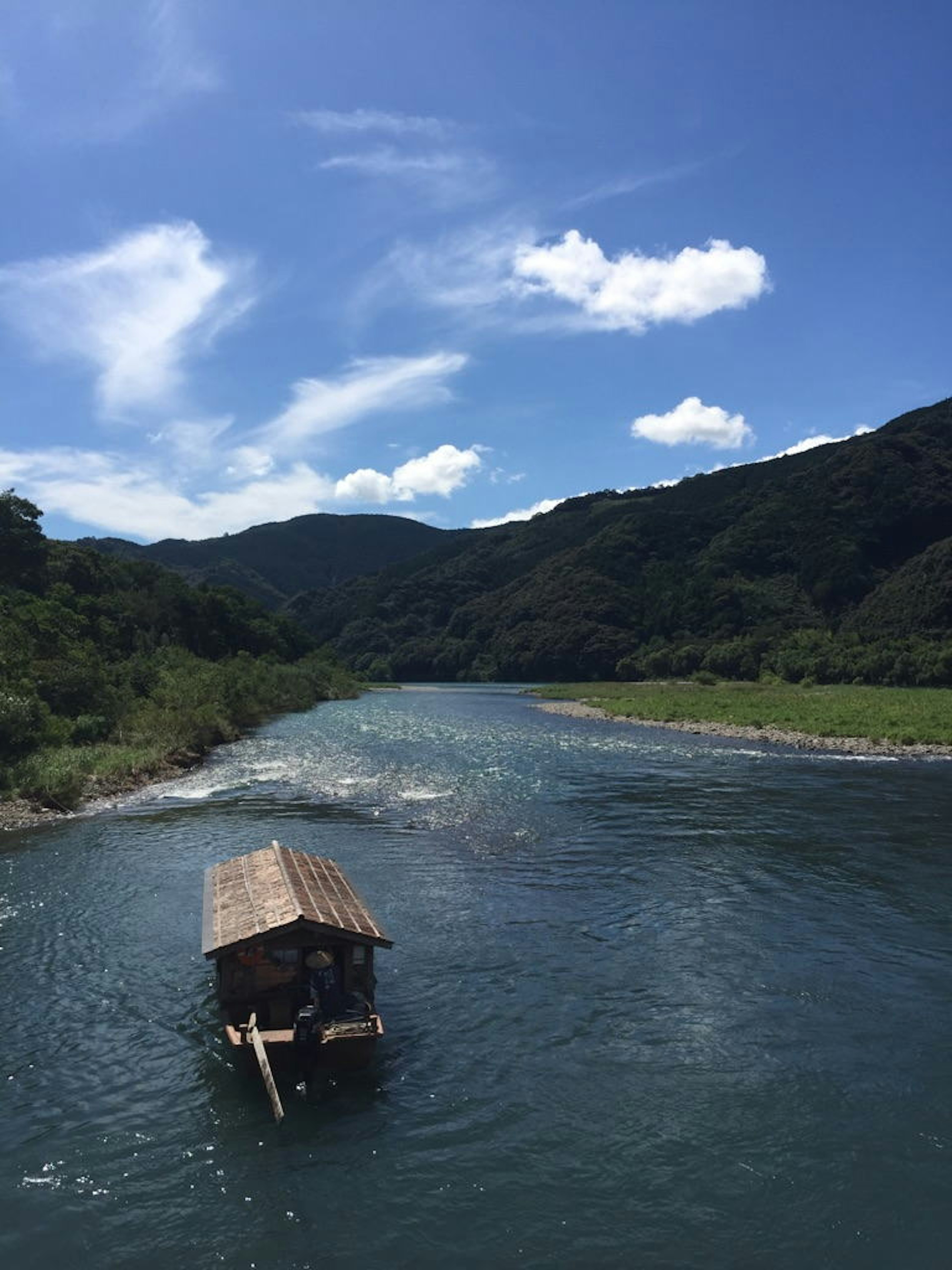 一艘小木船在藍天和背景山脈下沿著河流航行