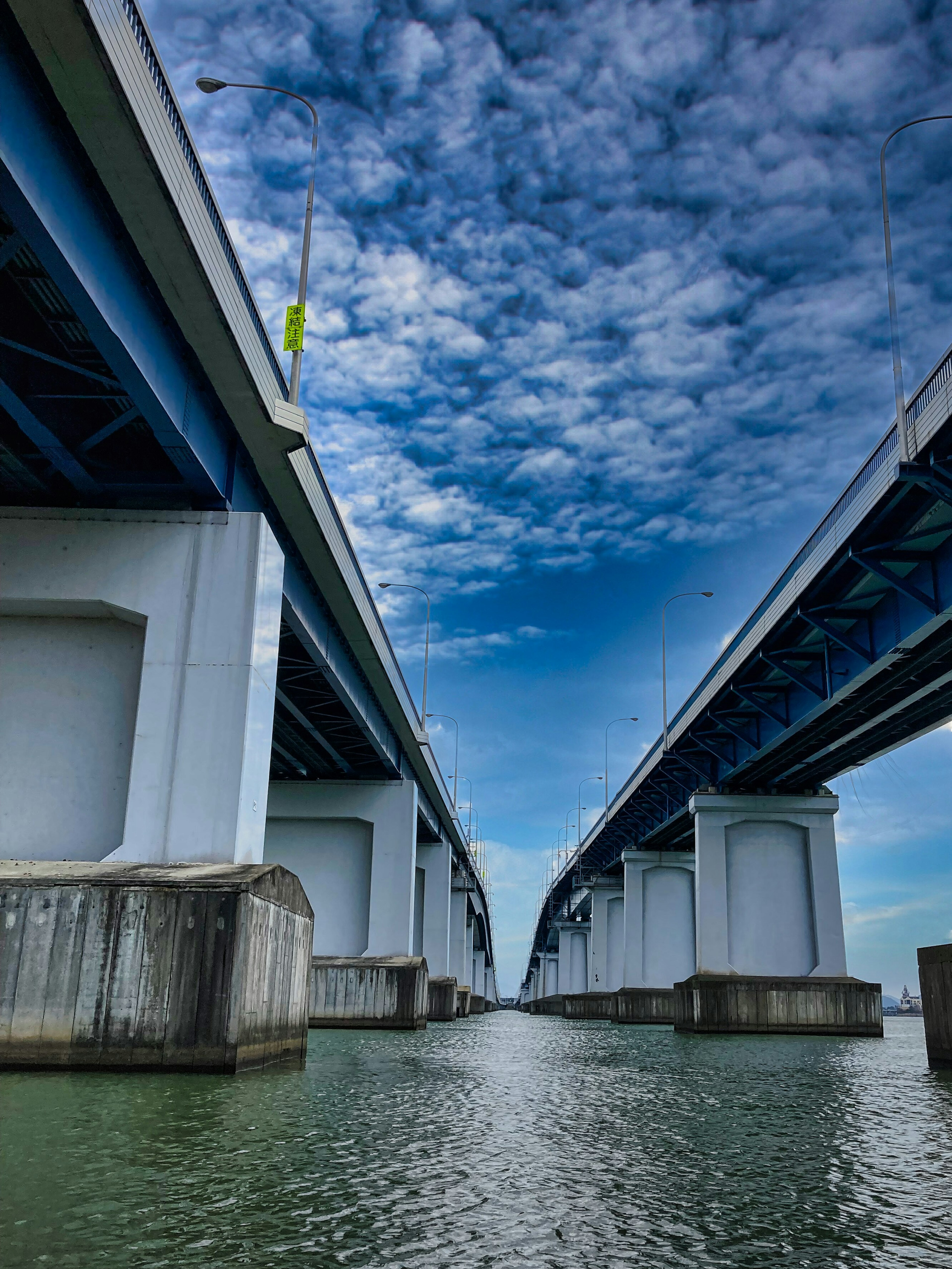 Pemandangan jembatan biru di atas air dengan langit berawan