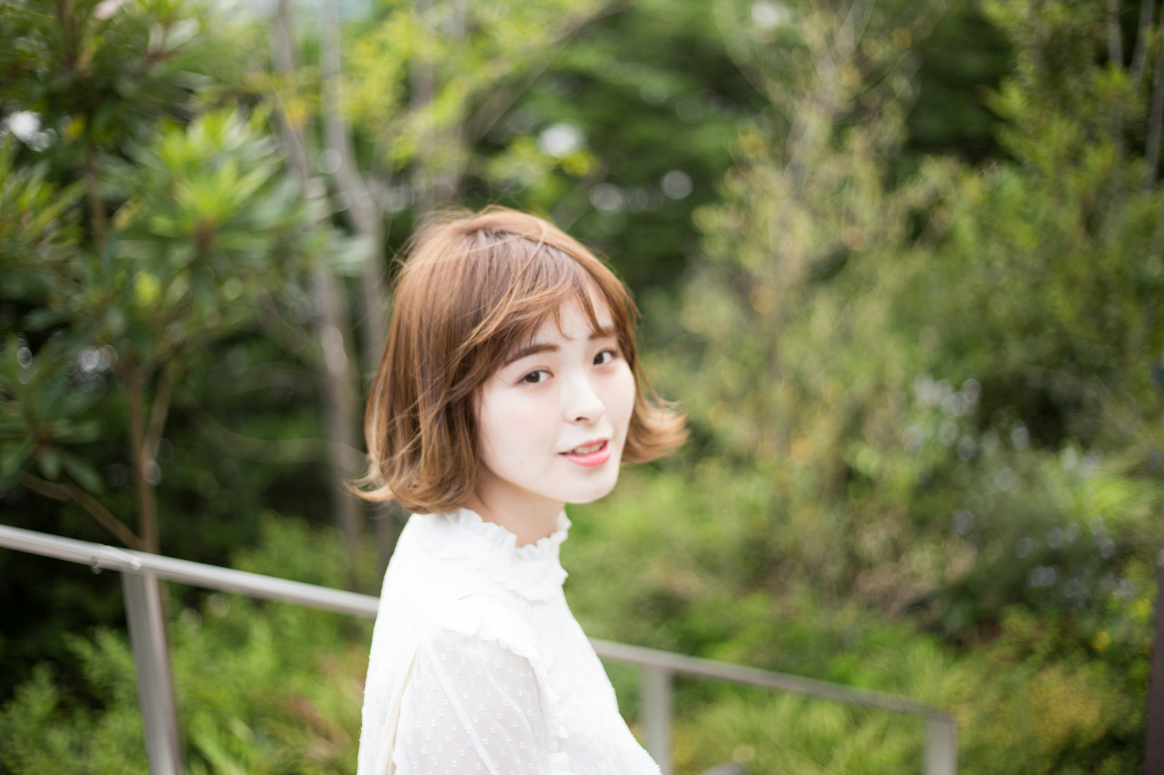 Portrait of a woman standing with a green background wearing a white blouse and short hair