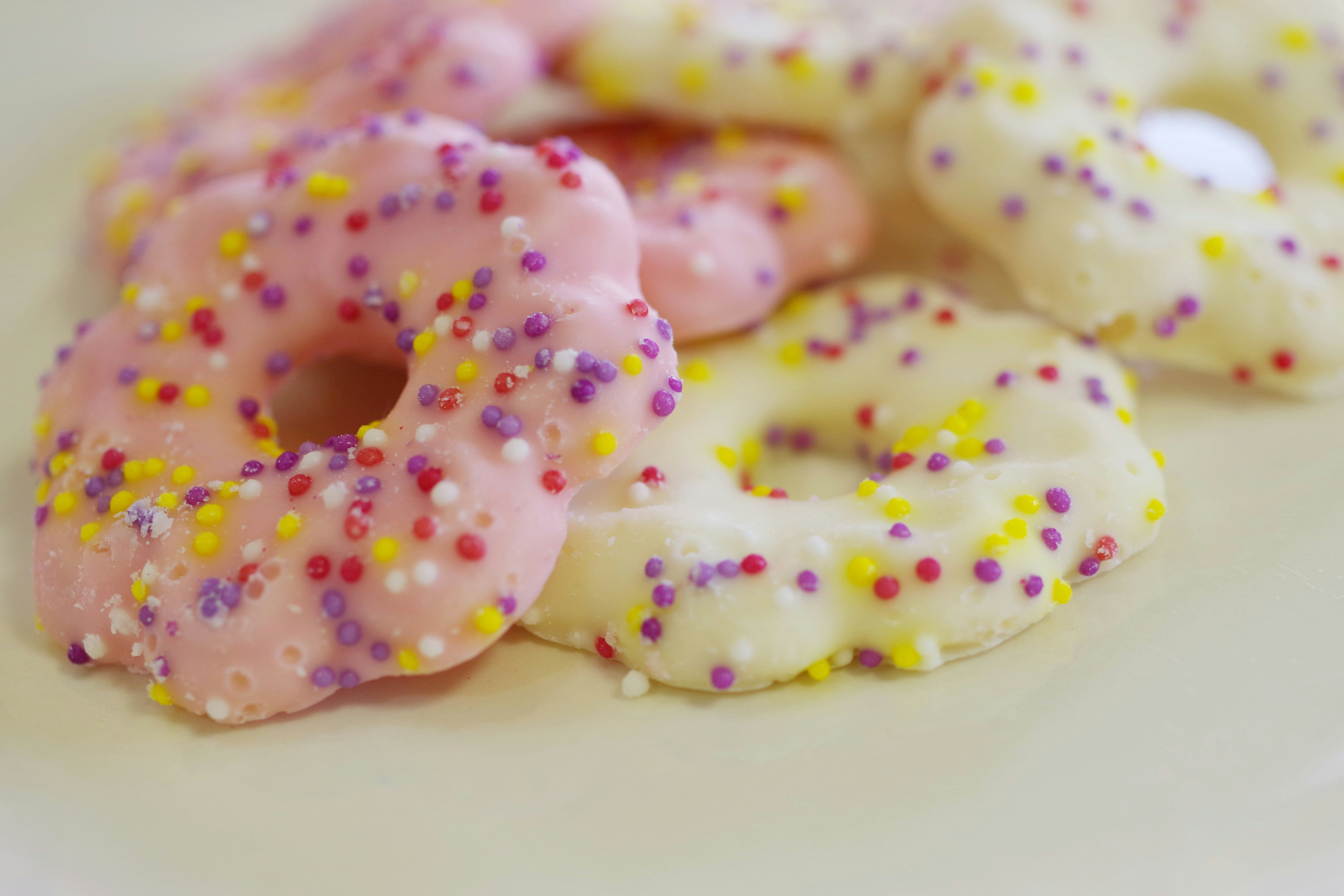 Makanan berbentuk donat berwarna pink dan putih yang ditaburi sprinkles berwarna