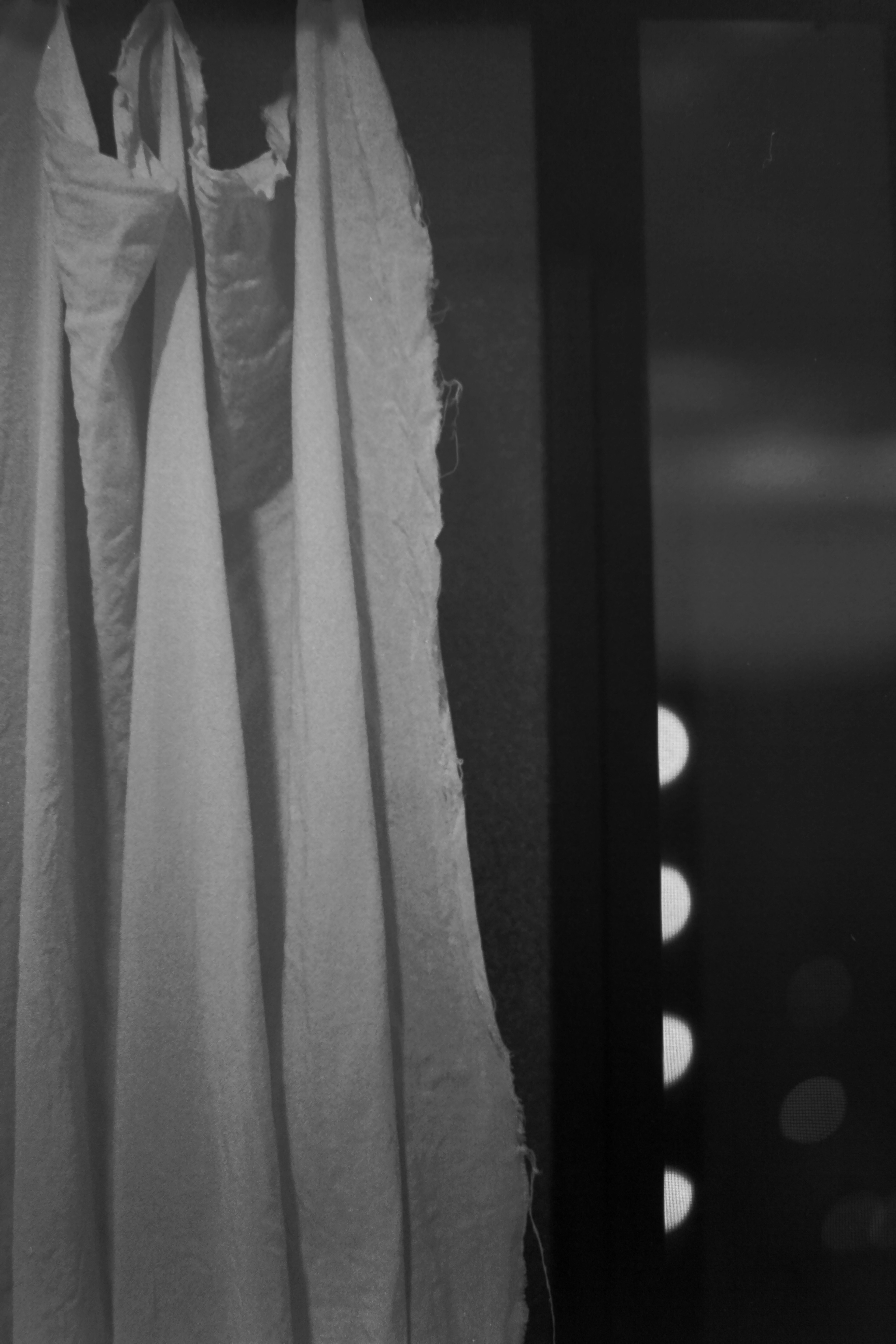 Black and white image of a white curtain hanging near a window with soft light spots visible outside