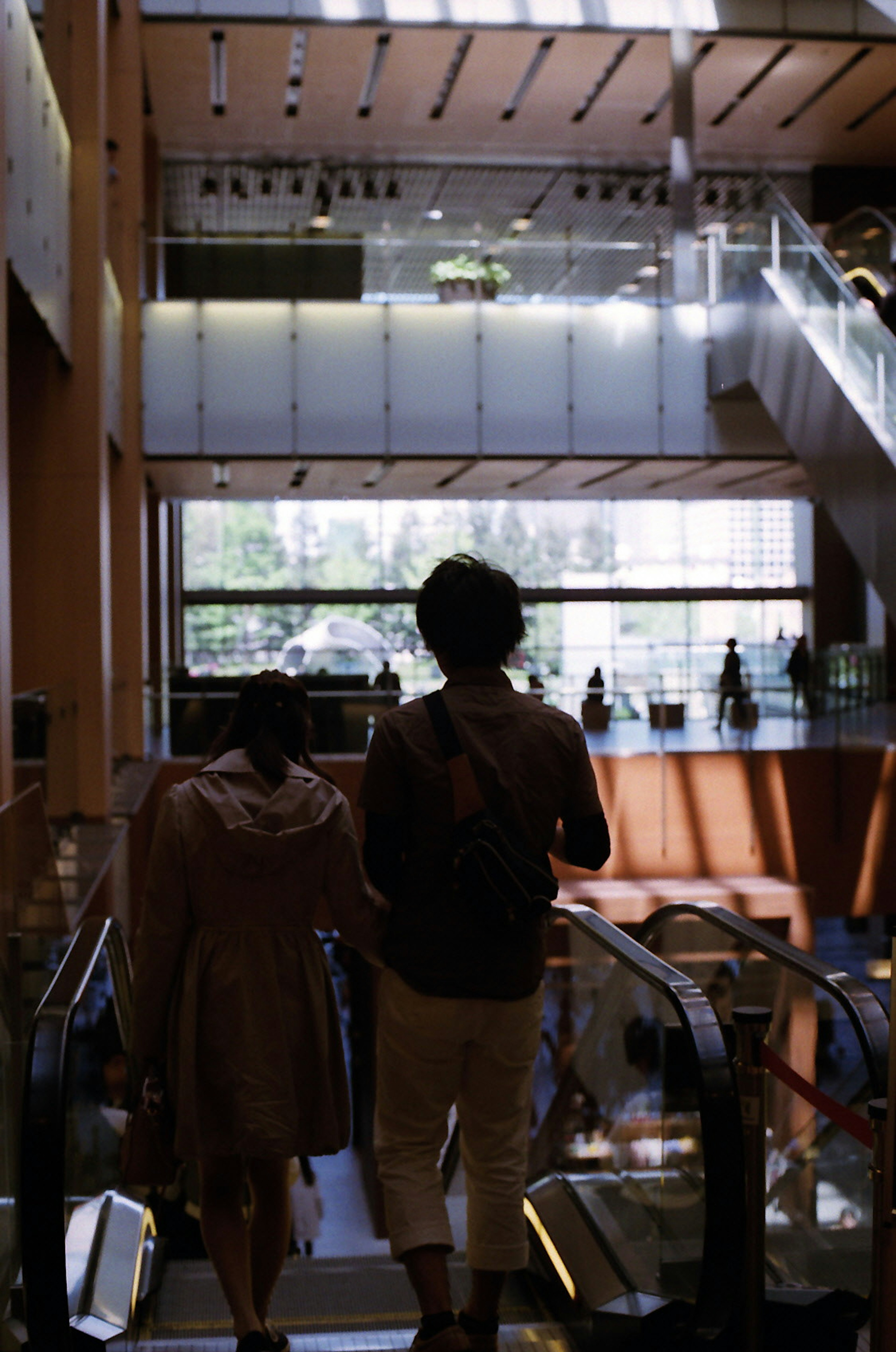 Dos personas bajando una escalera mecánica con ventanas brillantes al fondo