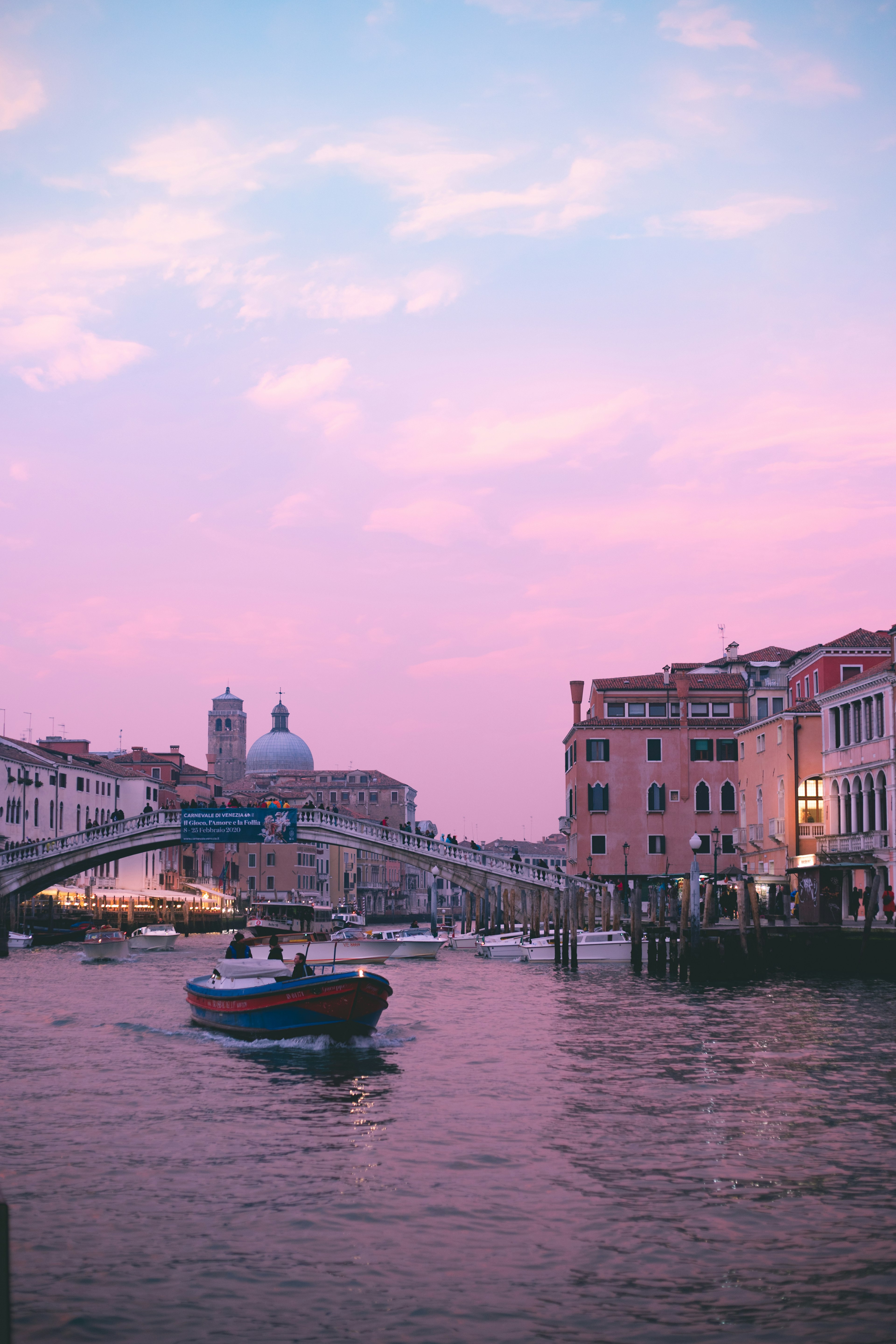 A boat navigating the Venetian canal under a colorful sunset sky with beautiful buildings