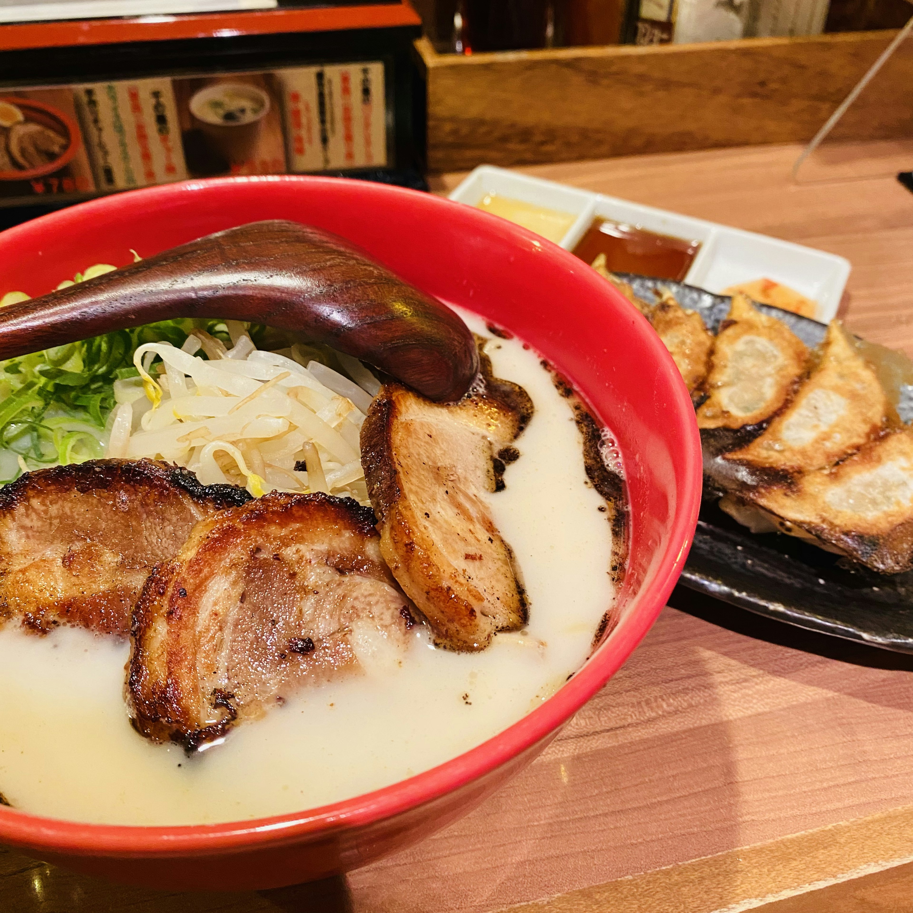 Ramen in una ciotola rossa con fette di maiale grigliato e un piatto di gyoza