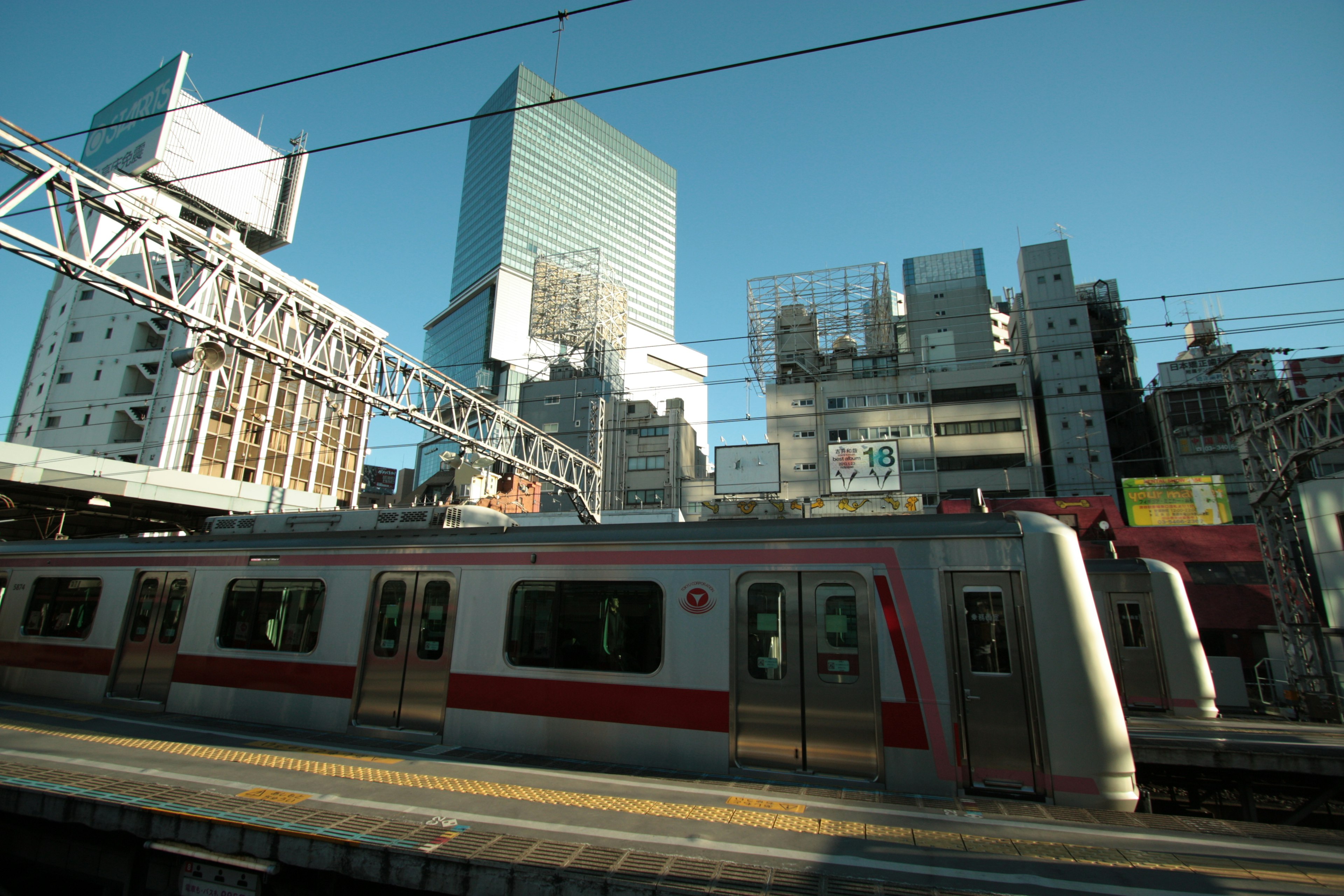 都市の鉄道駅に停車中の赤い電車と高層ビル群