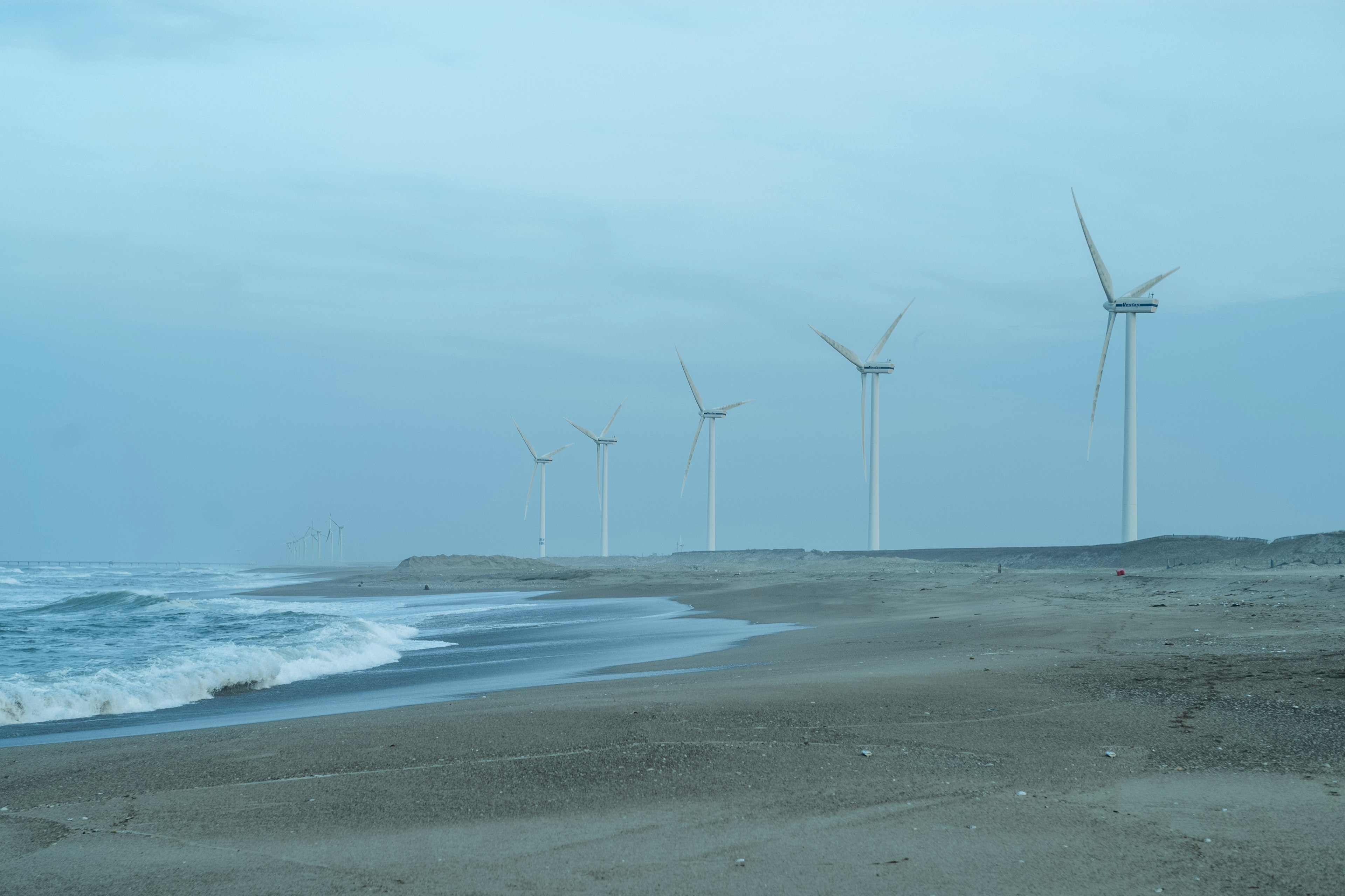 海岸に立つ風力発電機の列と穏やかな波