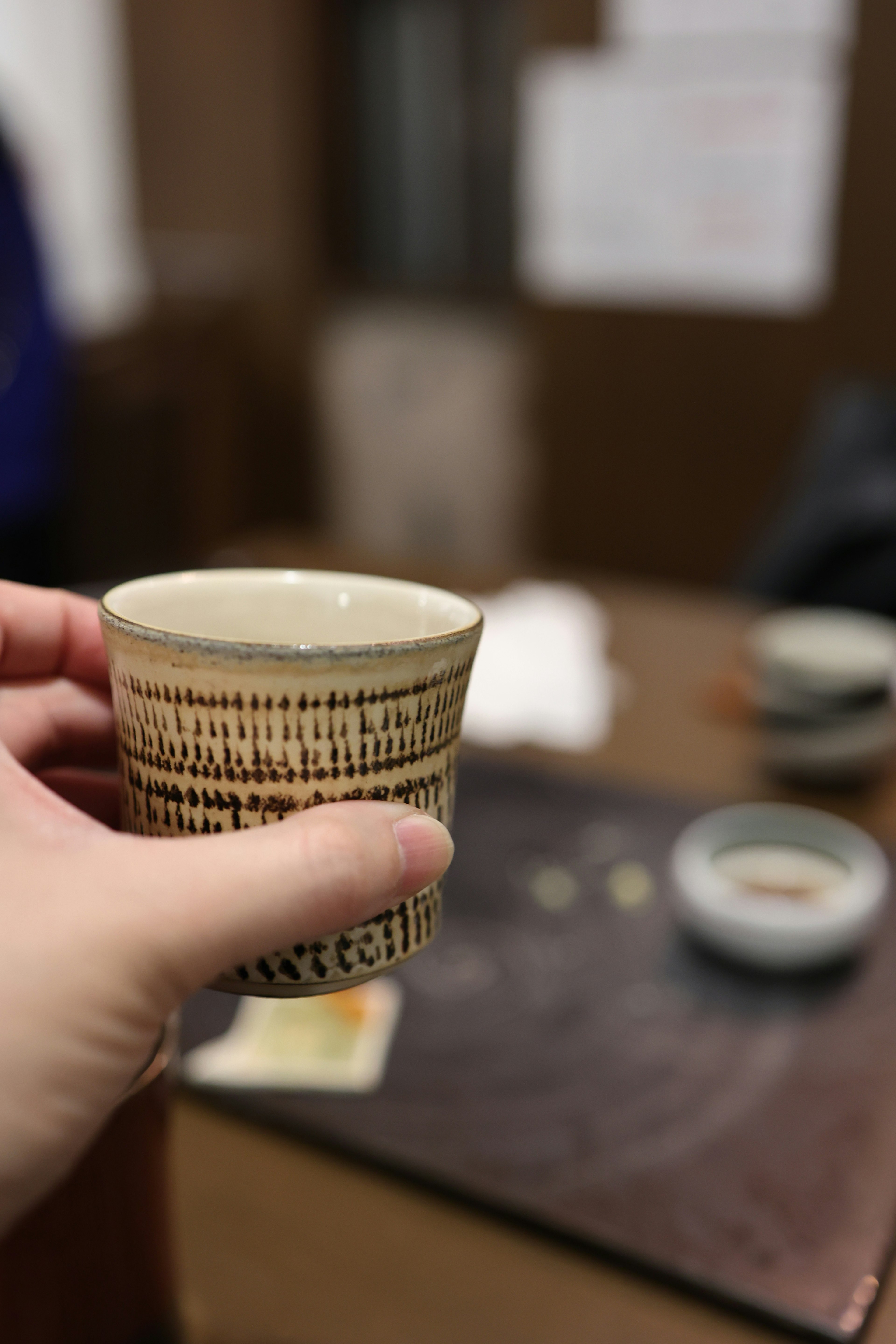 Hand hält eine Keramiktasse mit verschwommenem Tischhintergrund