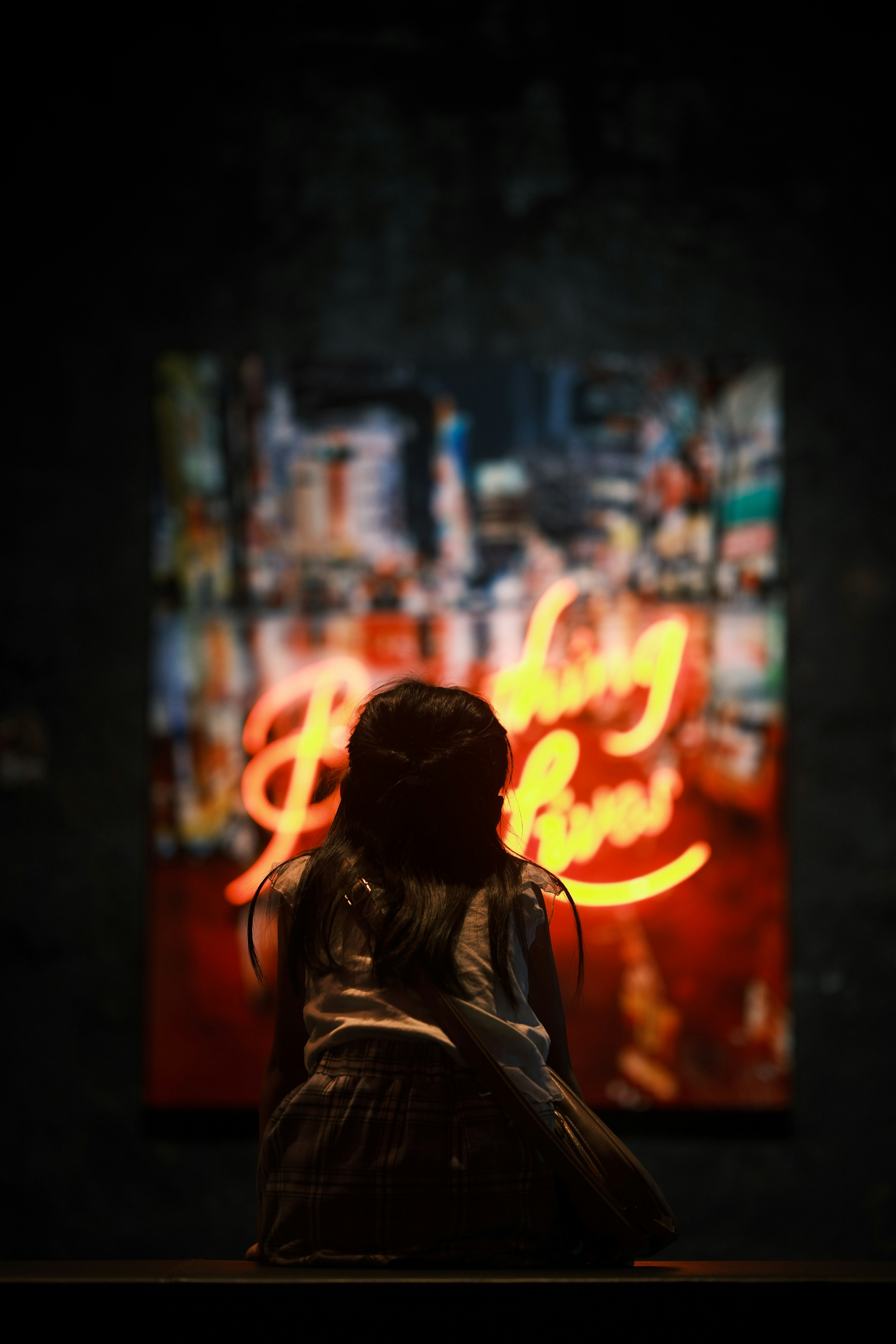 Silhouette of a woman admiring neon artwork against a dark background