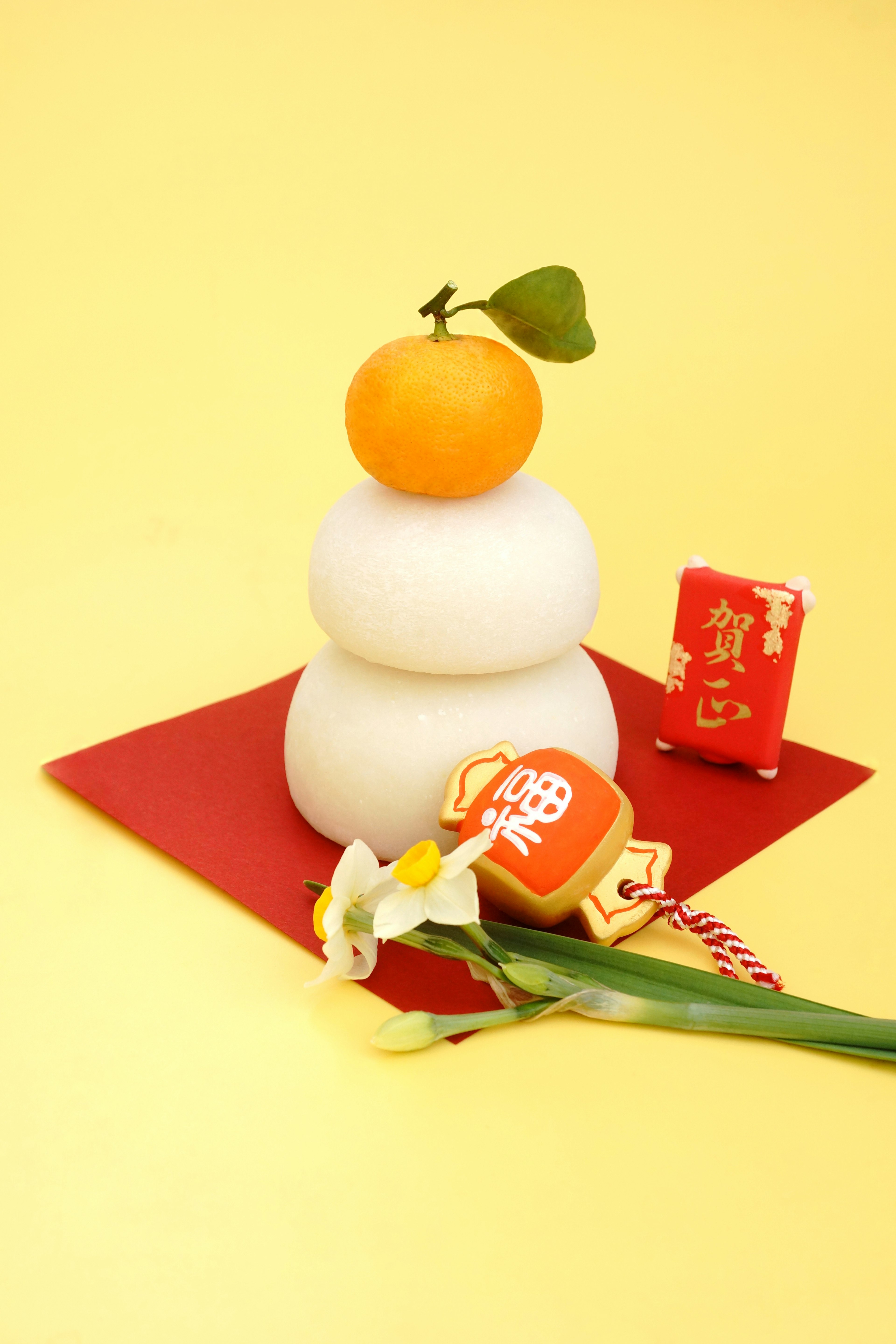 Three stacked white rice cakes topped with a mandarin orange on a yellow background