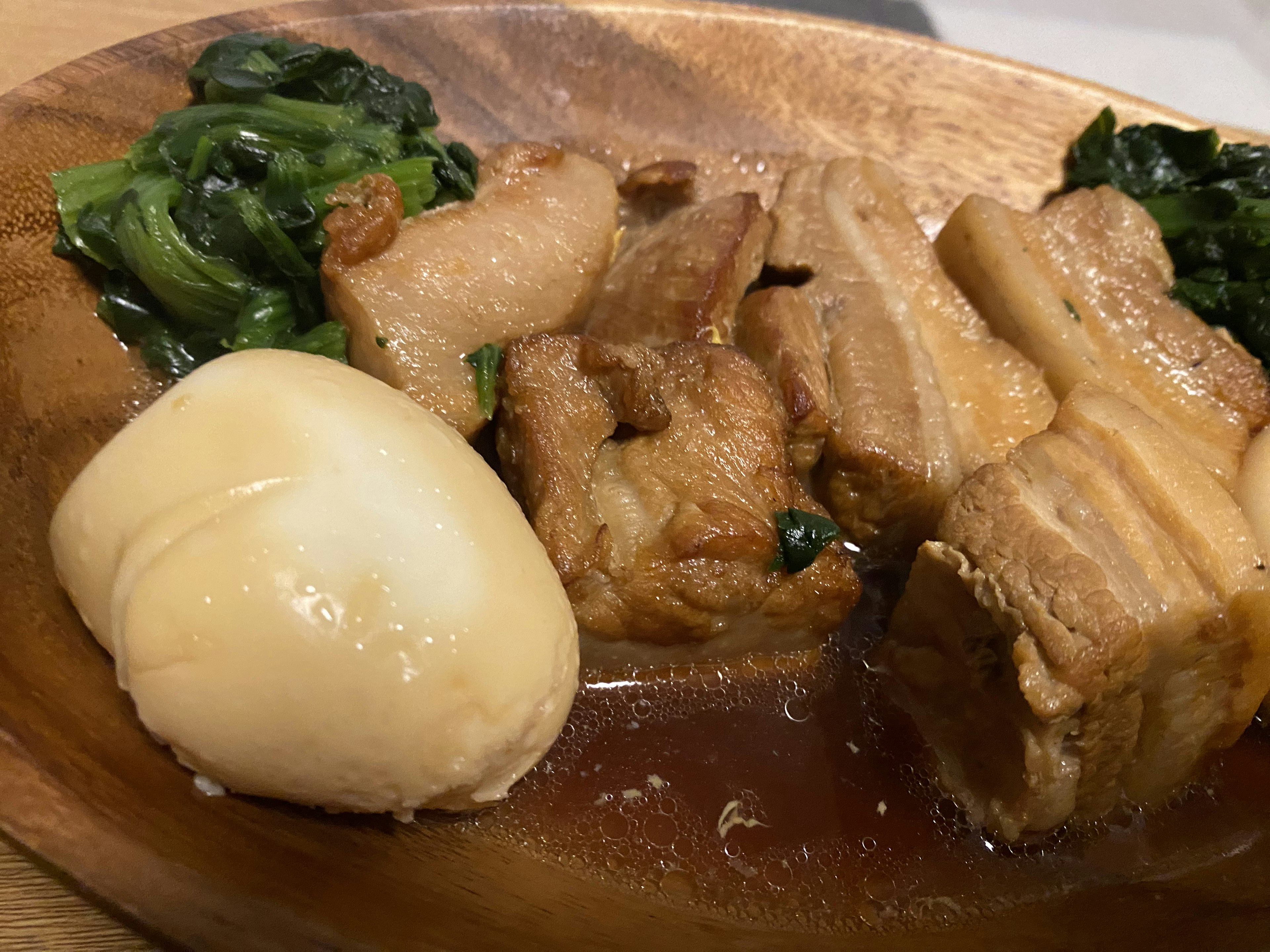 A wooden plate featuring pork belly, boiled potatoes, and sautéed greens