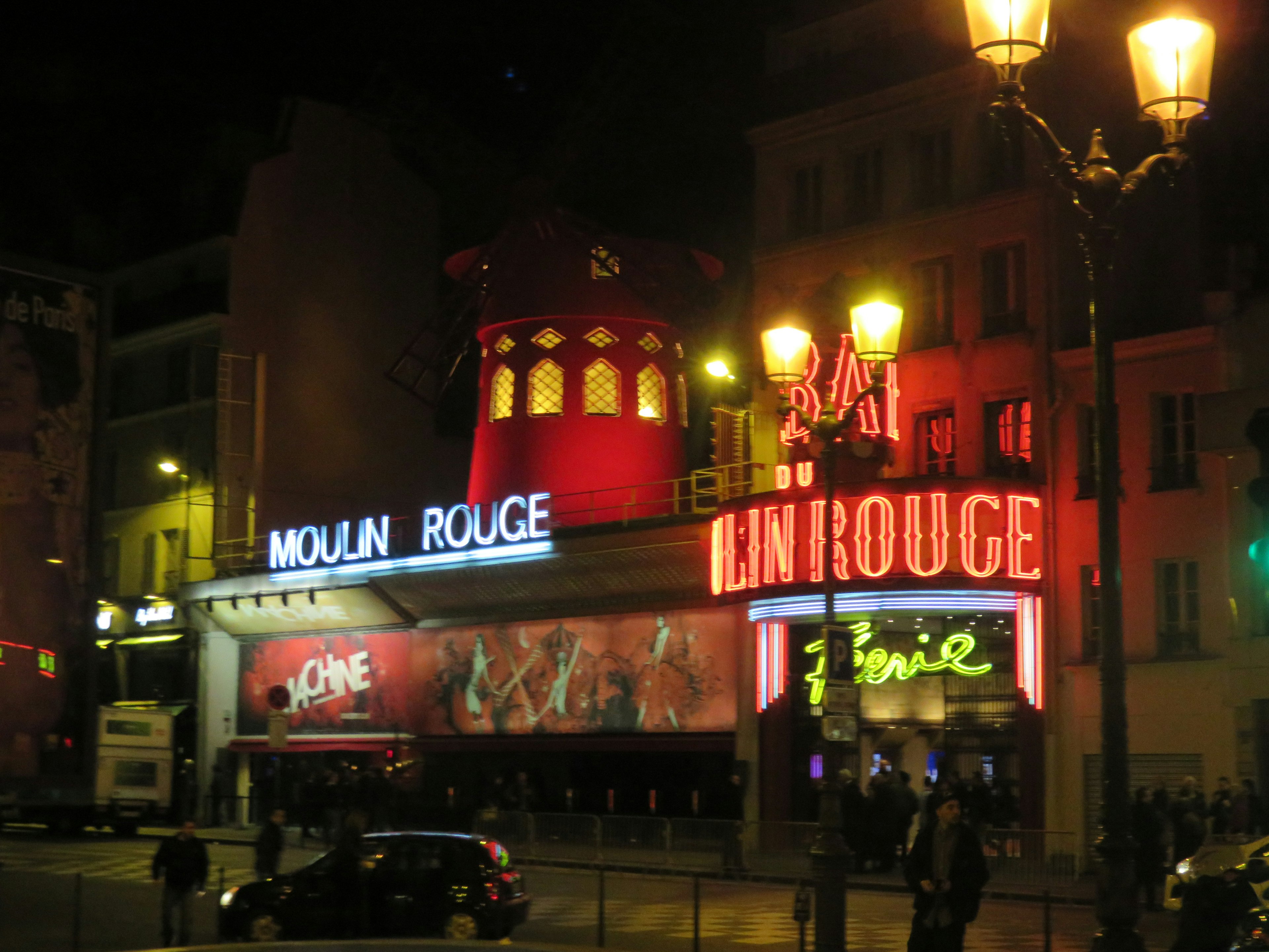 Vista notturna del Moulin Rouge con luci al neon rosse e l'iconica struttura del mulino